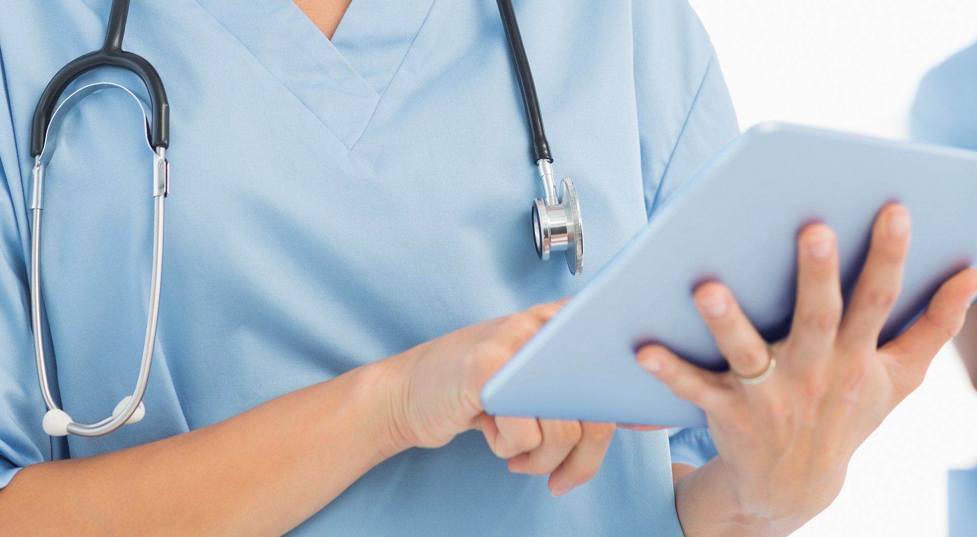 A nurse with a stethoscope around her neck is using a tablet computer.
