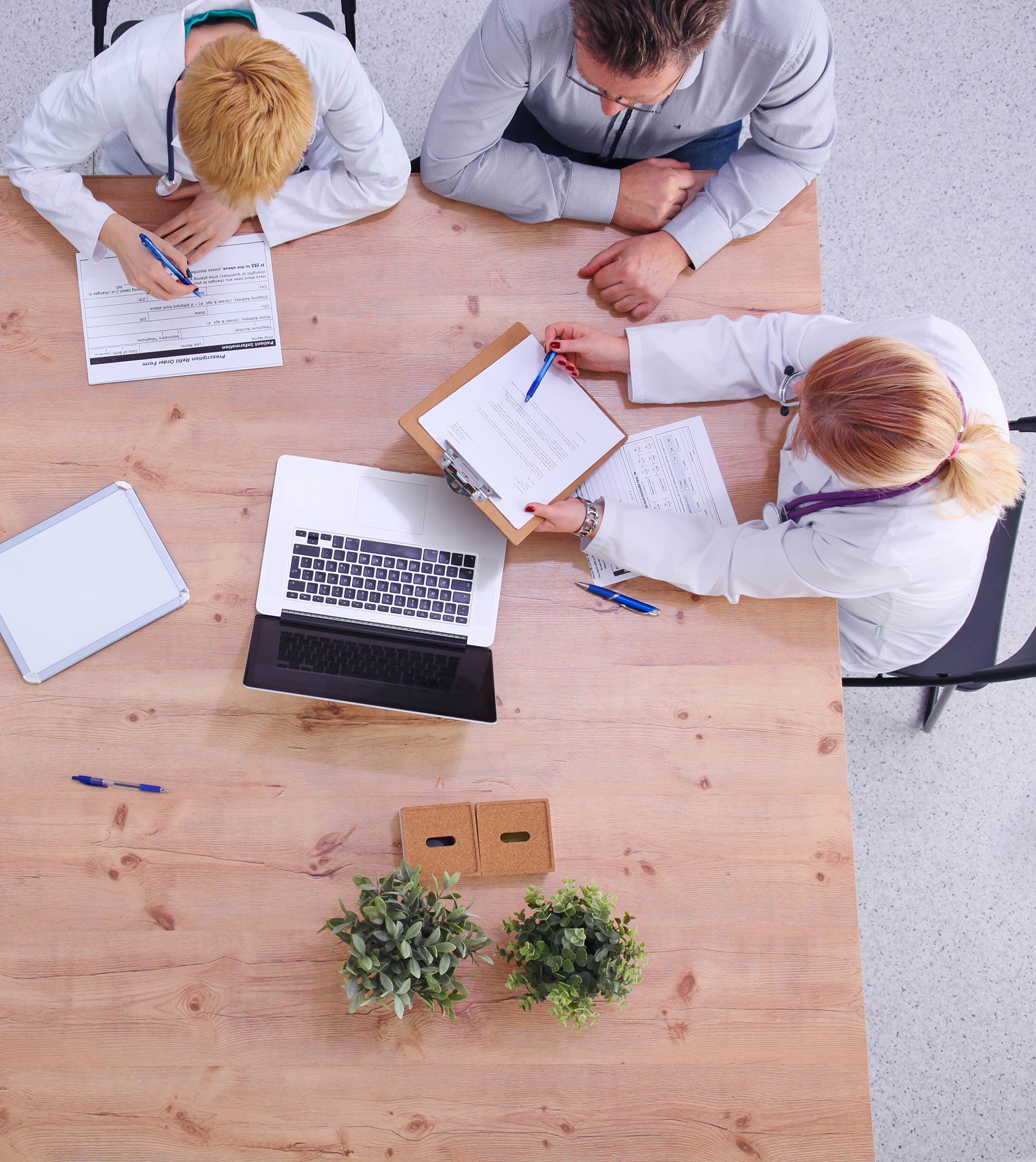 A group of doctors are sitting at a table with papers and a laptop