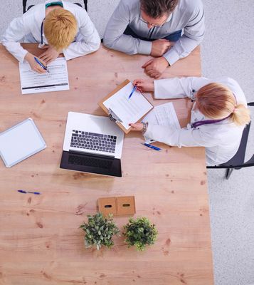 Three medical professionals and a patient at a wooden table; discussing paperwork.
