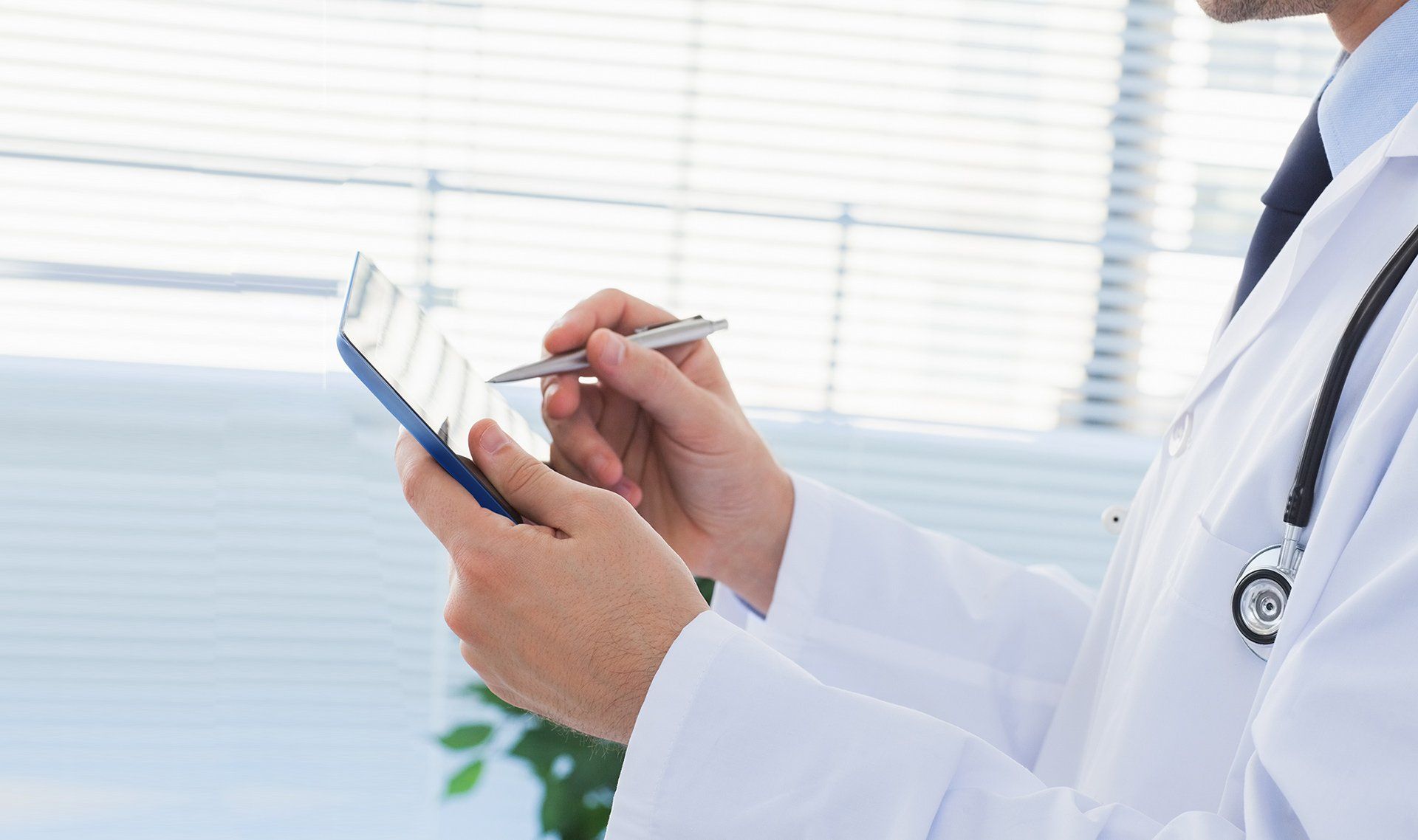 A doctor is writing on a clipboard with a pen.