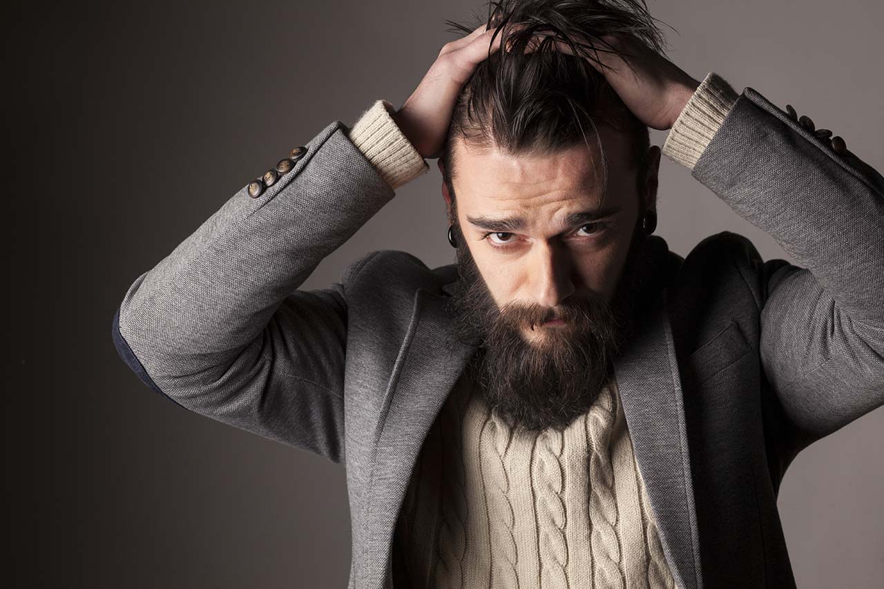 A man with a beard is holding his hair in a bun.