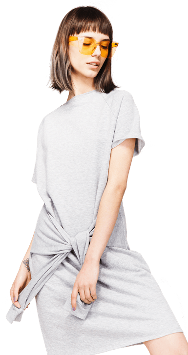 A woman wearing a grey dress and yellow sunglasses is standing on a white background.