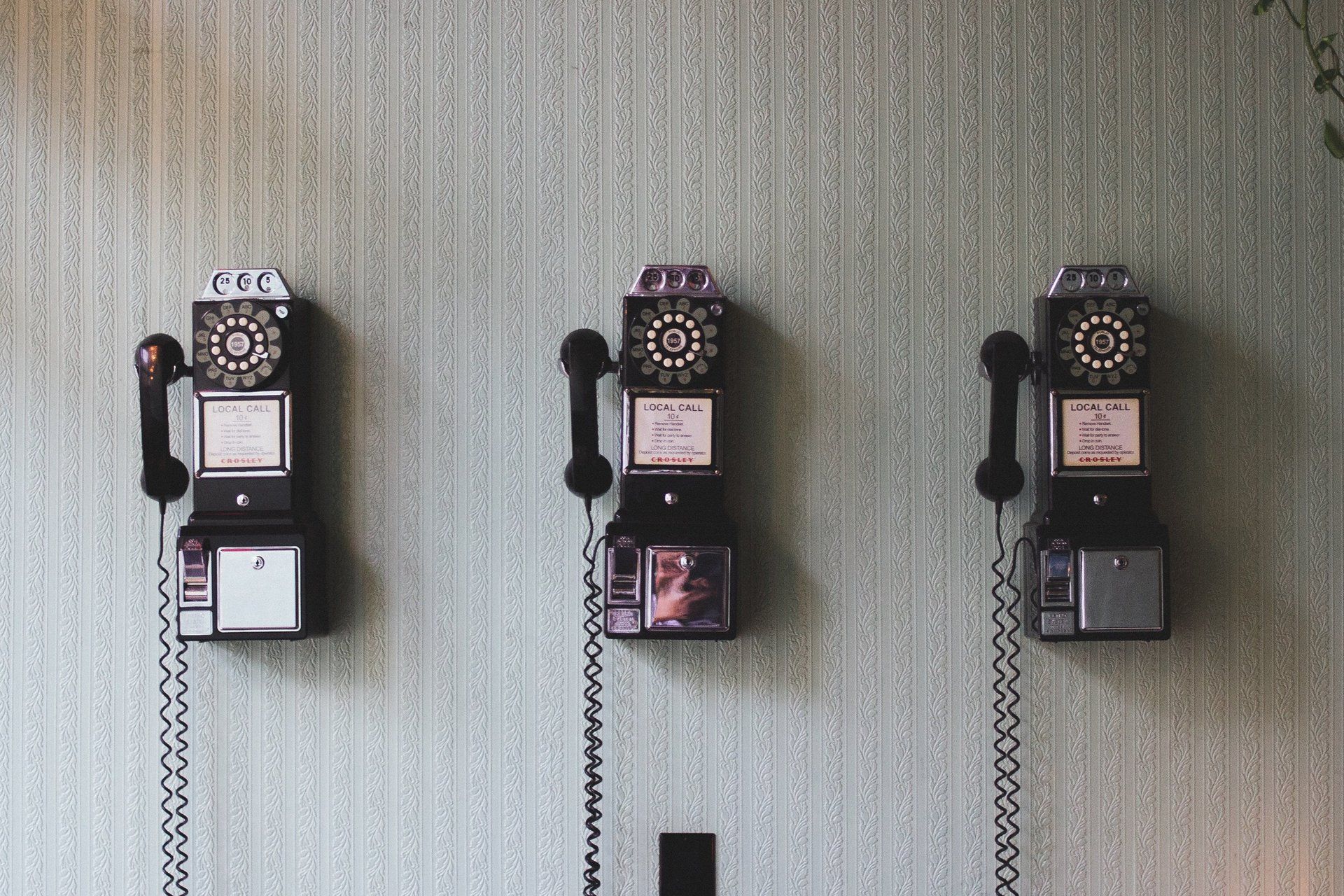 Three old pay phones are hanging on a wall.