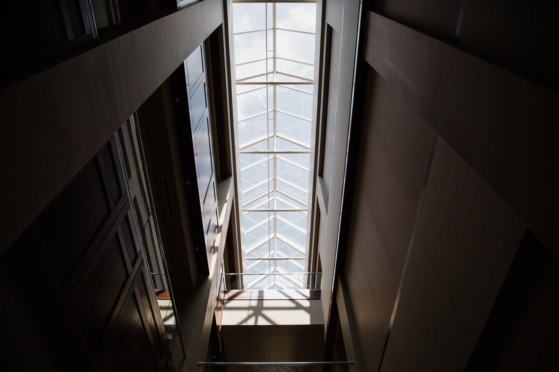 Tall skylit atrium with dark walls and a bright glass roof overhead