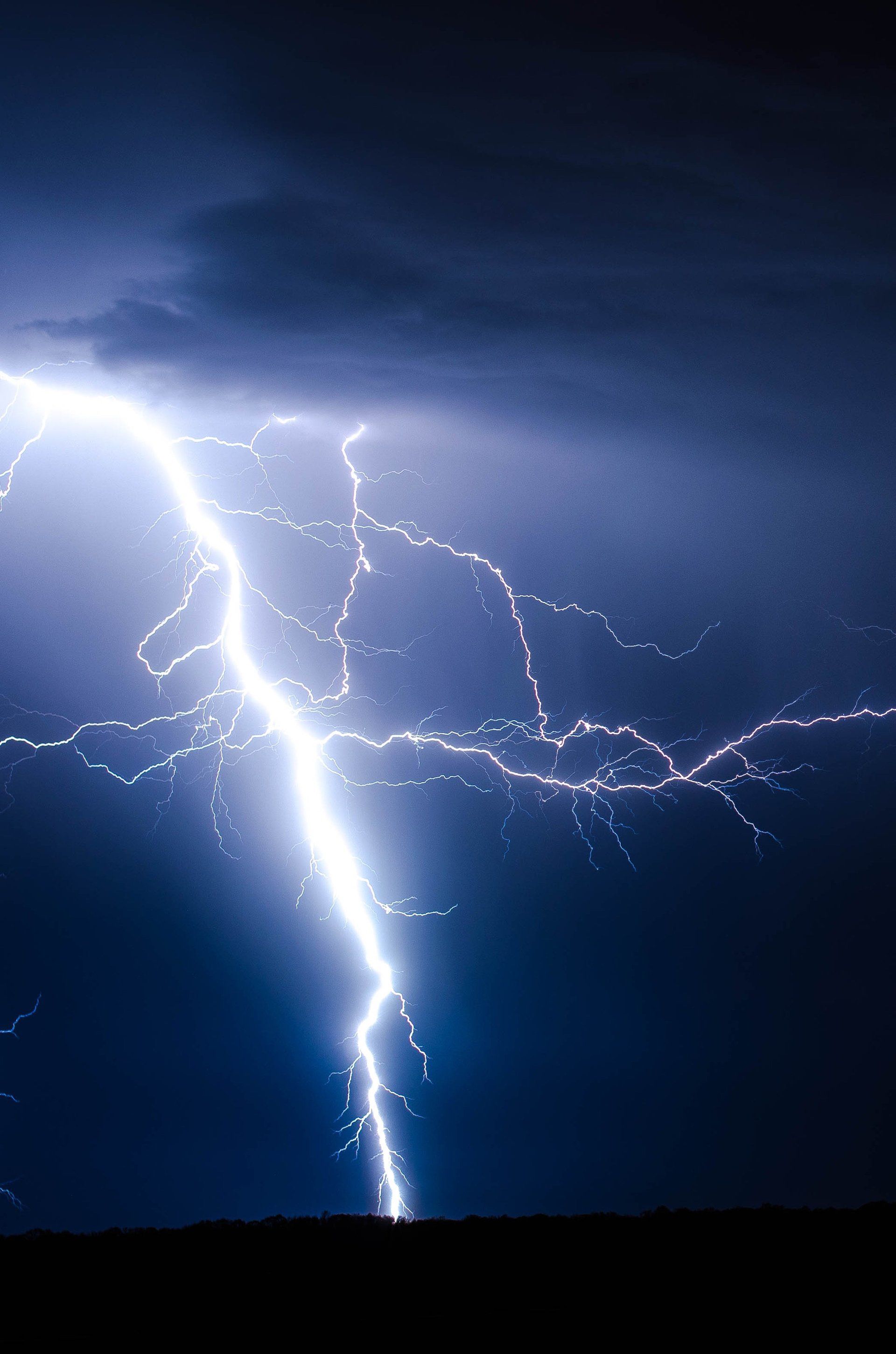 Bright lightning bolt striking a dark night sky above the horizon