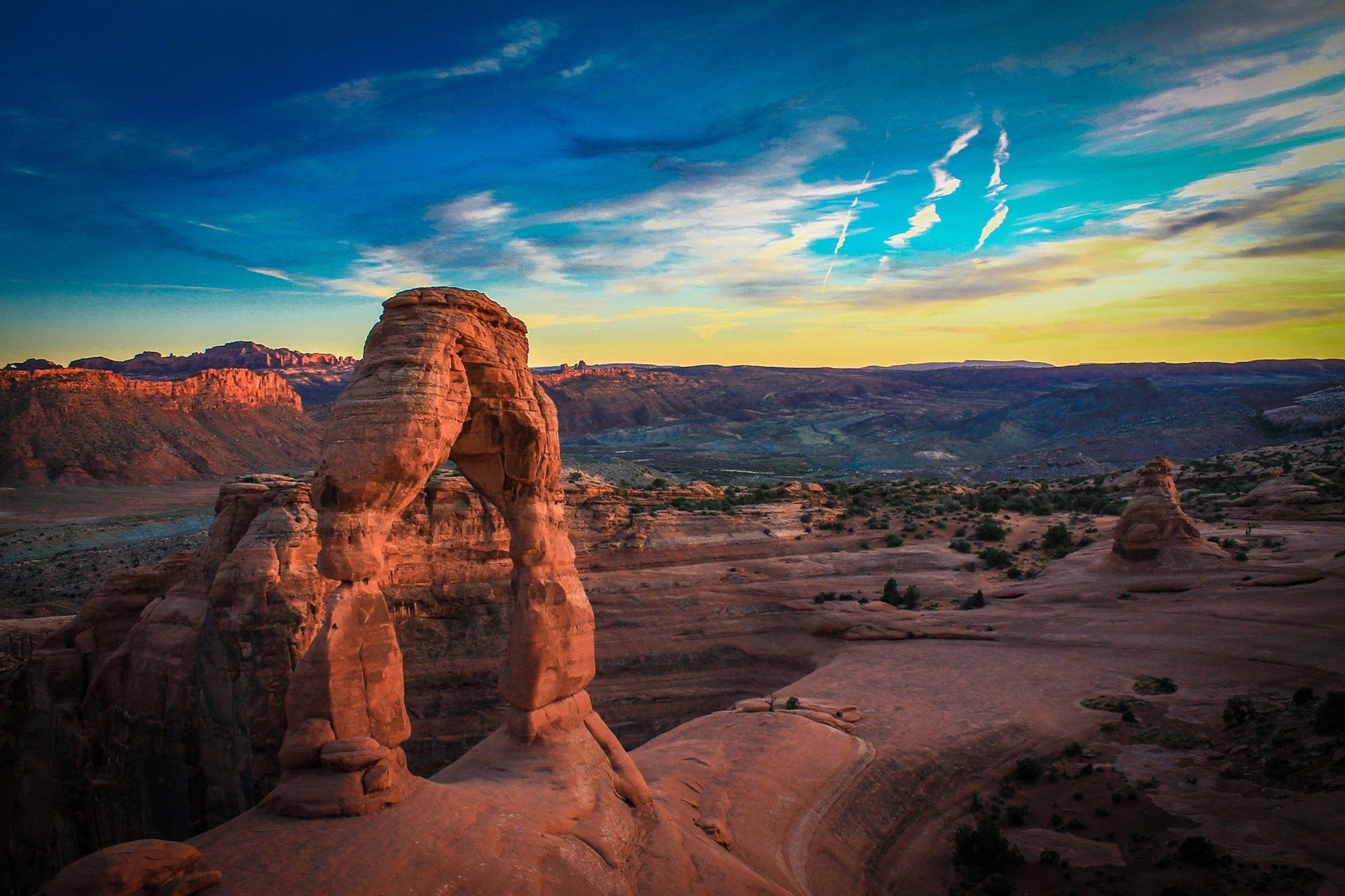 Delicate Arch in Arches National Park, Utah, stands against a vibrant sunset sky over a vast, rocky desert landscape.