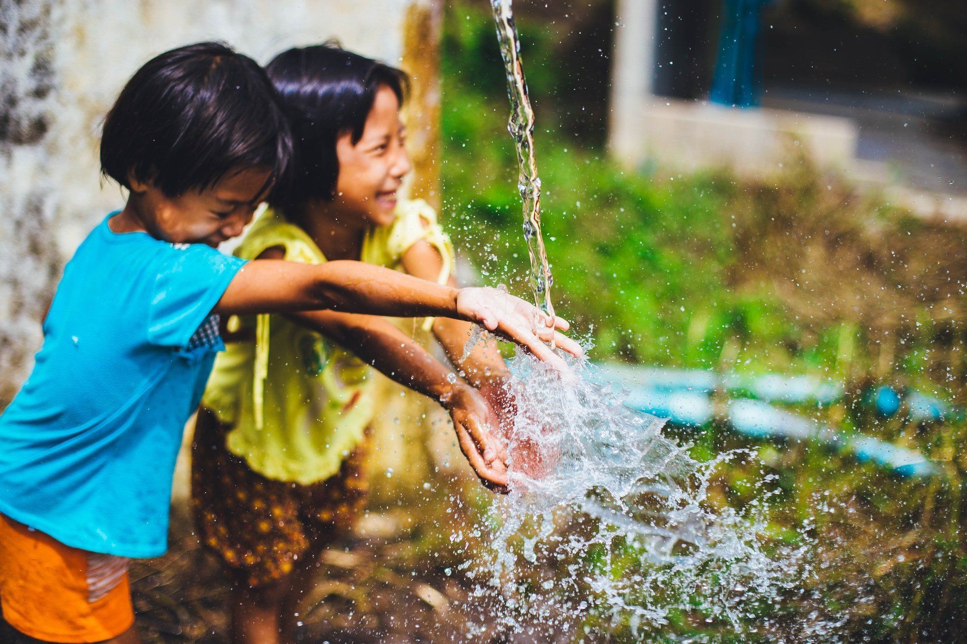 Two children playing with water, splashing, and smiling outdoors.