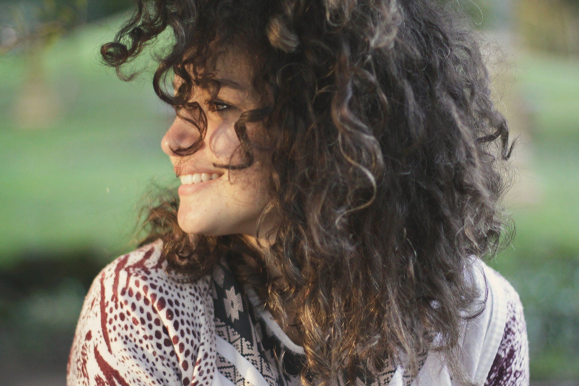 A woman with curly hair smiles towards the left side of the frame.