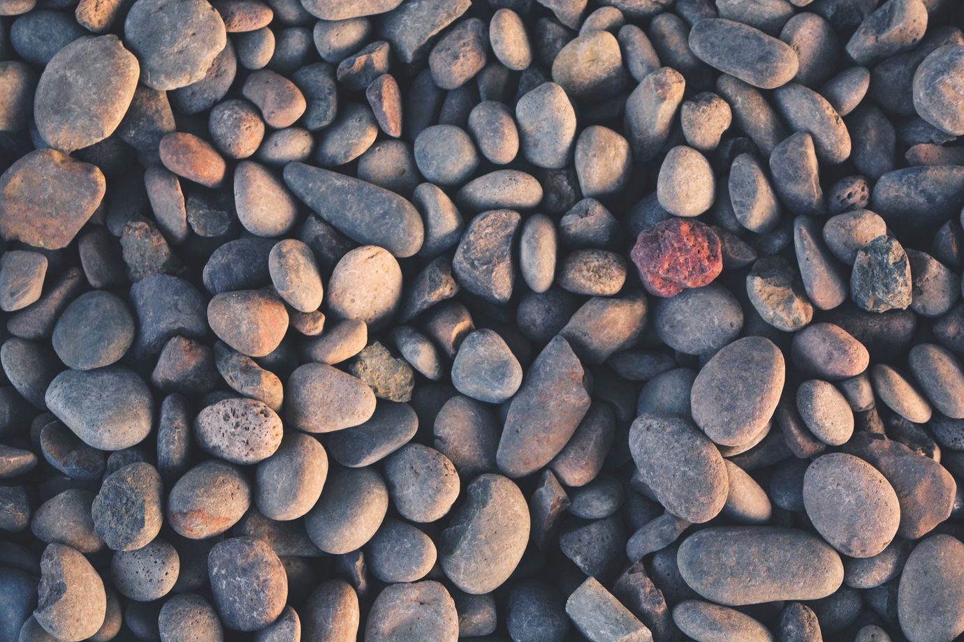 A pile of rocks with one red rock in the middle.