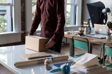 A man is standing next to a table holding a cardboard box.