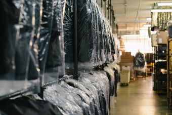 Garments covered in plastic hang in a dim clothing warehouse aisle