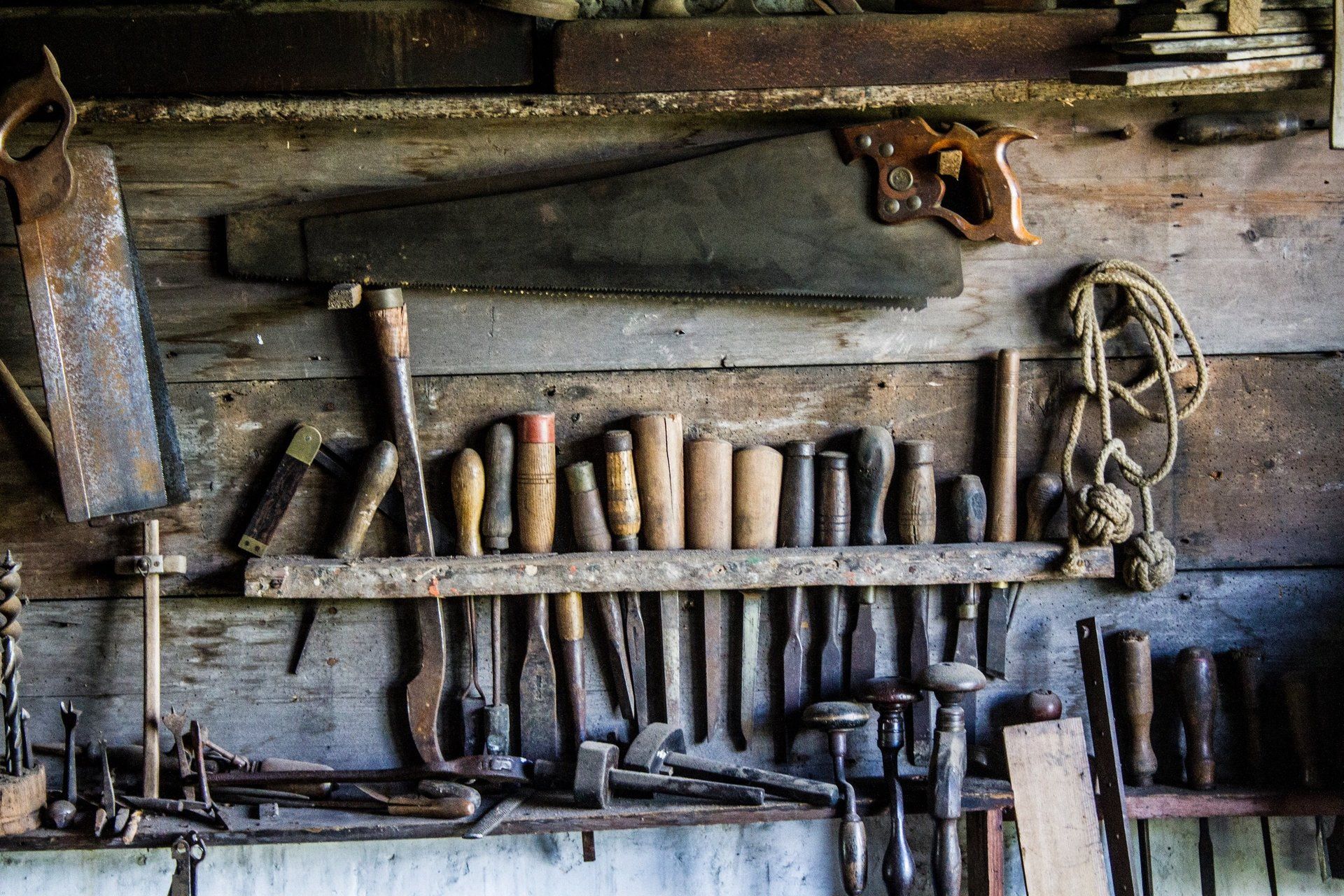A bunch of tools are hanging on a wooden wall.