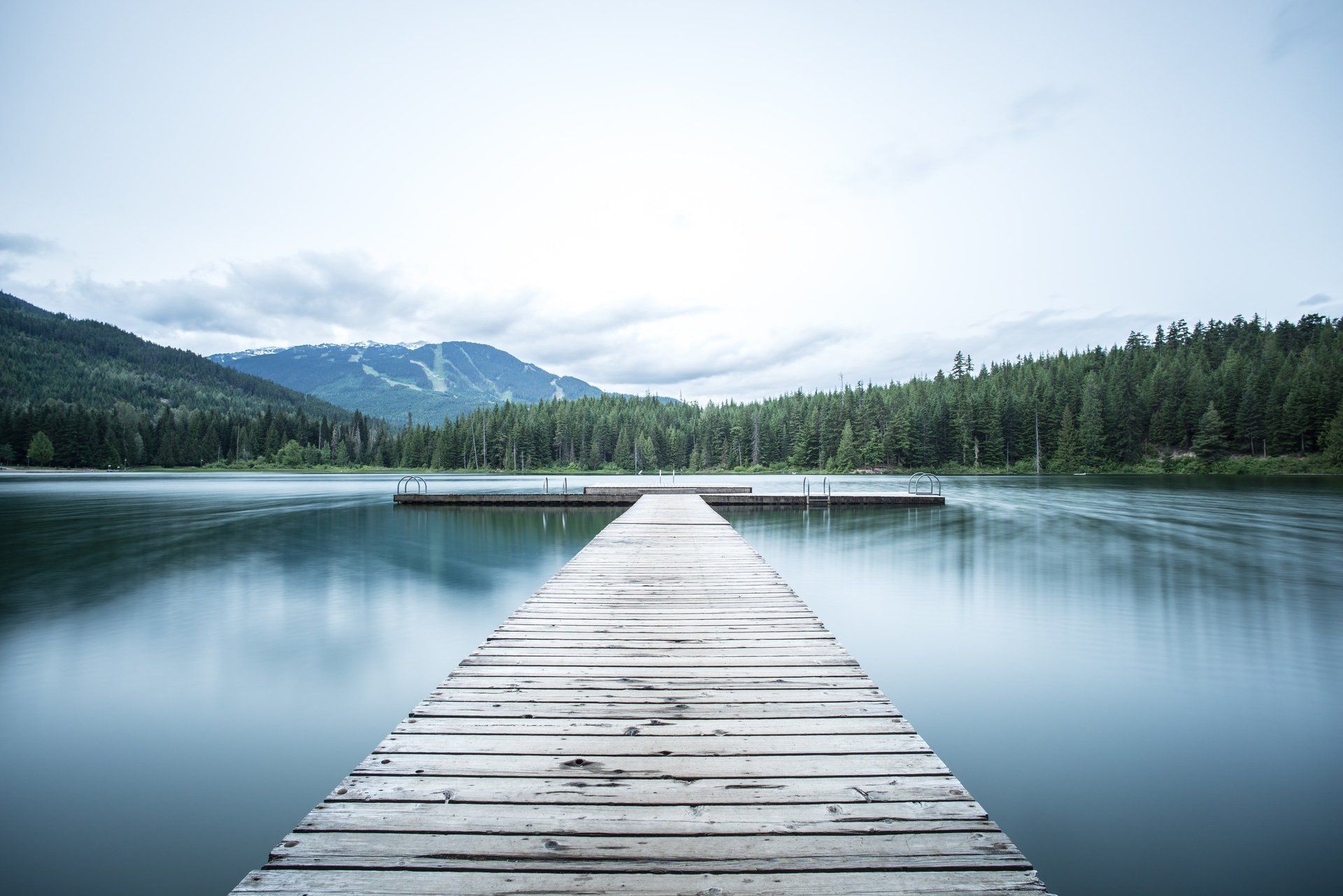 A wooden dock leading into a lake with mountains in the background.