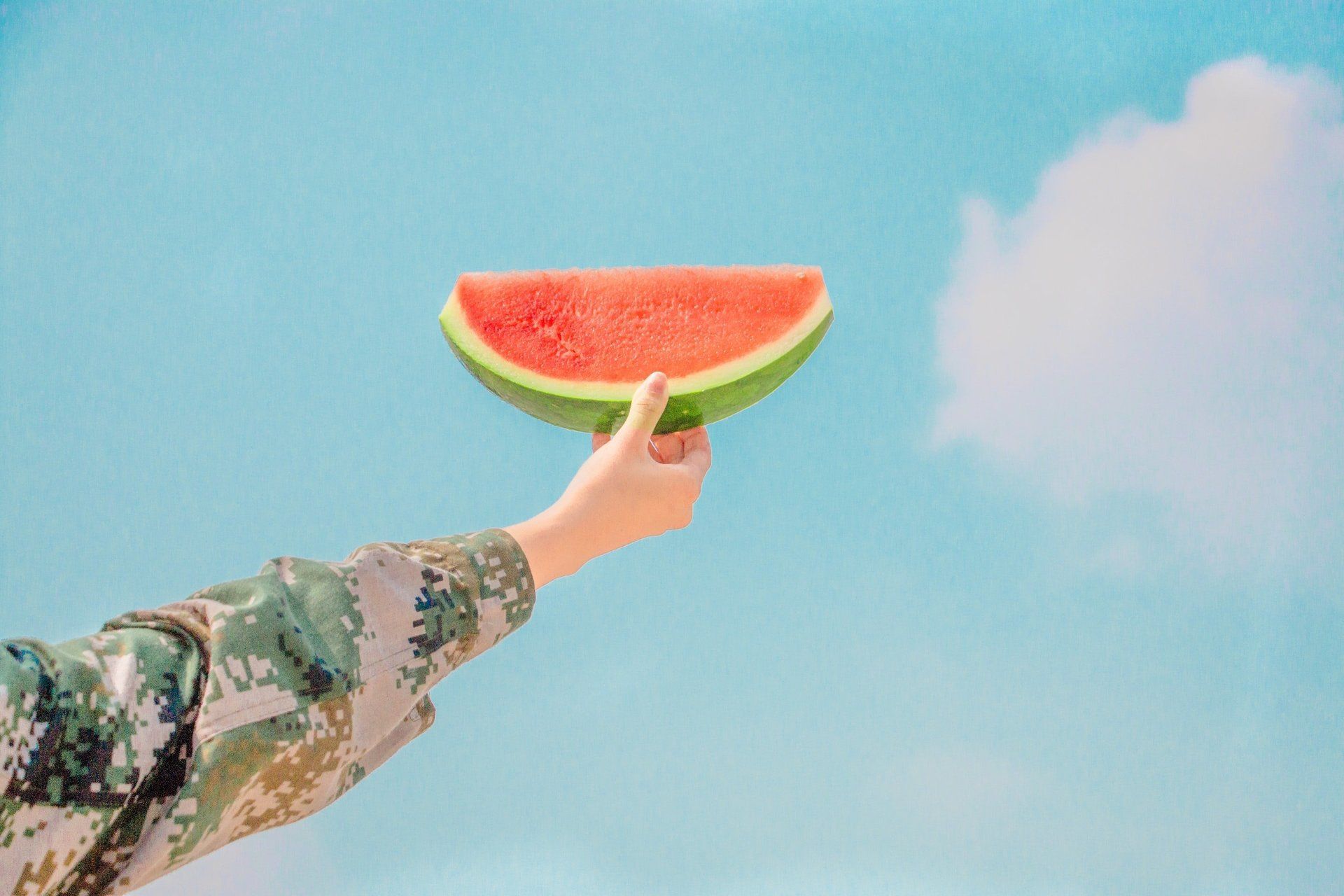 A person is holding a slice of watermelon in front of a blue sky.