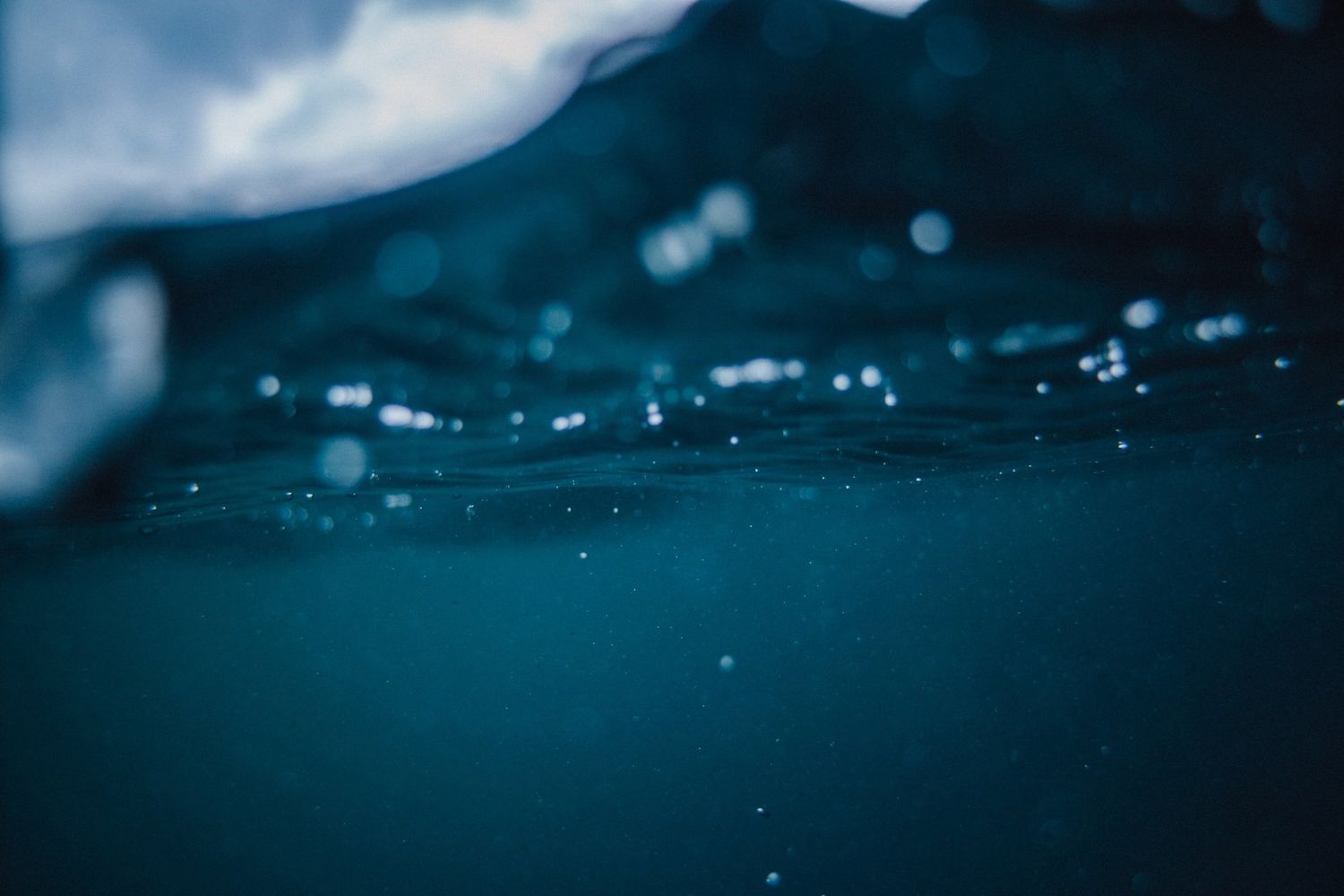 Underwater view of a dark blue ocean surface with floating bubbles and light reflections