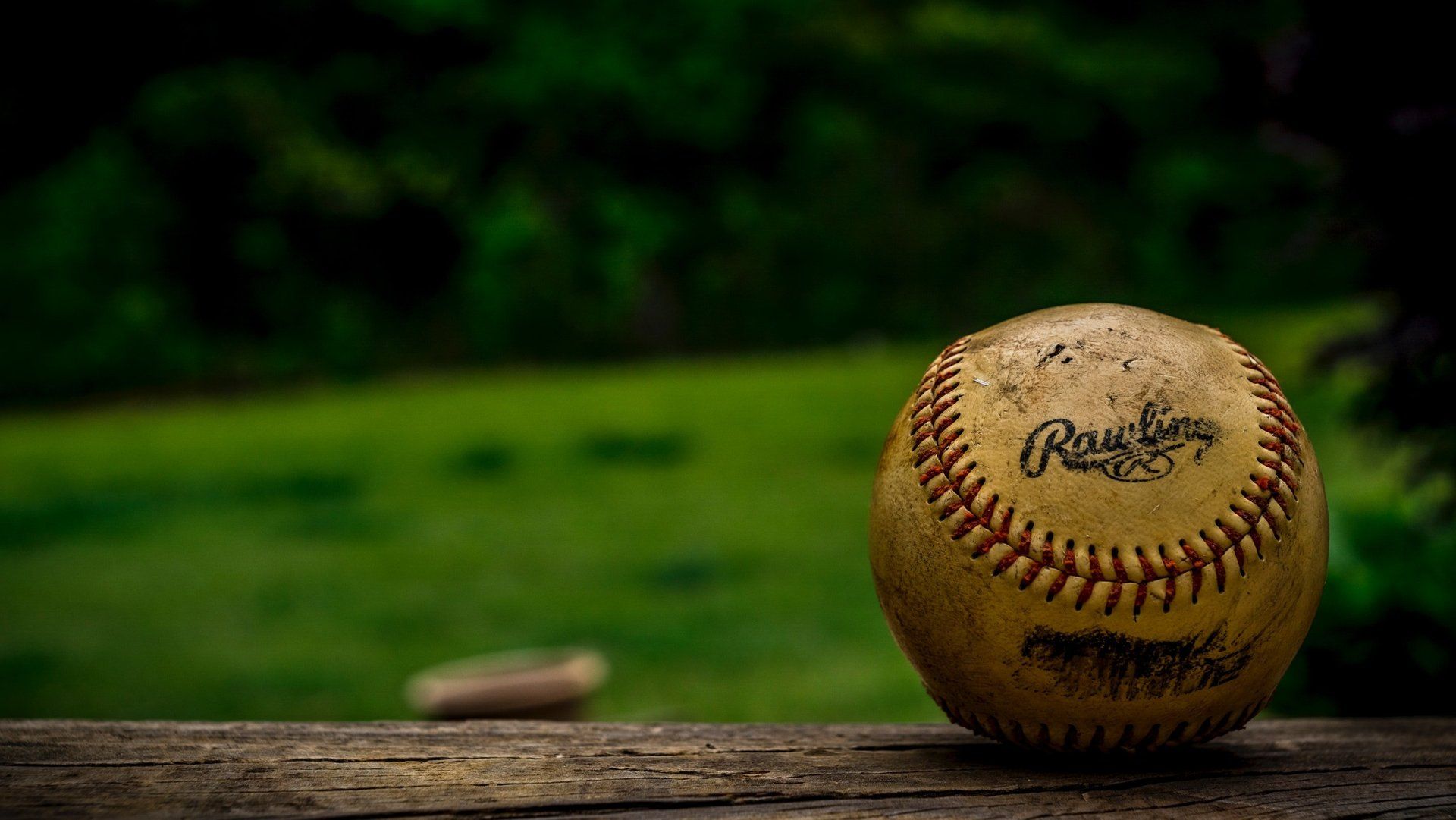 A worn baseball on a wooden surface with a blurred green field in the background.
