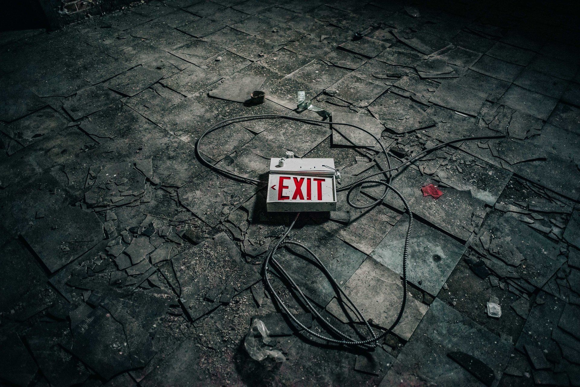 Damaged EXIT sign lying on cracked pavement with tangled wires and scattered debris