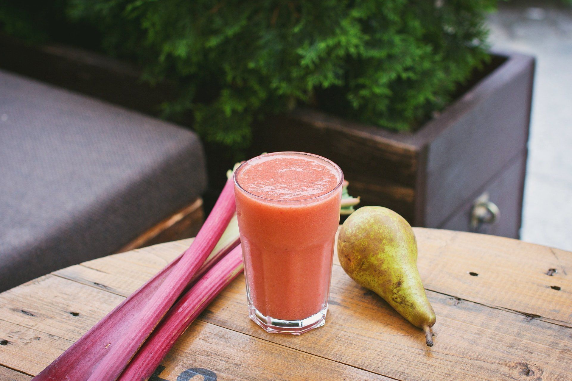 Glass of pink rhubarb pear juice with stalks and pear on wooden table.