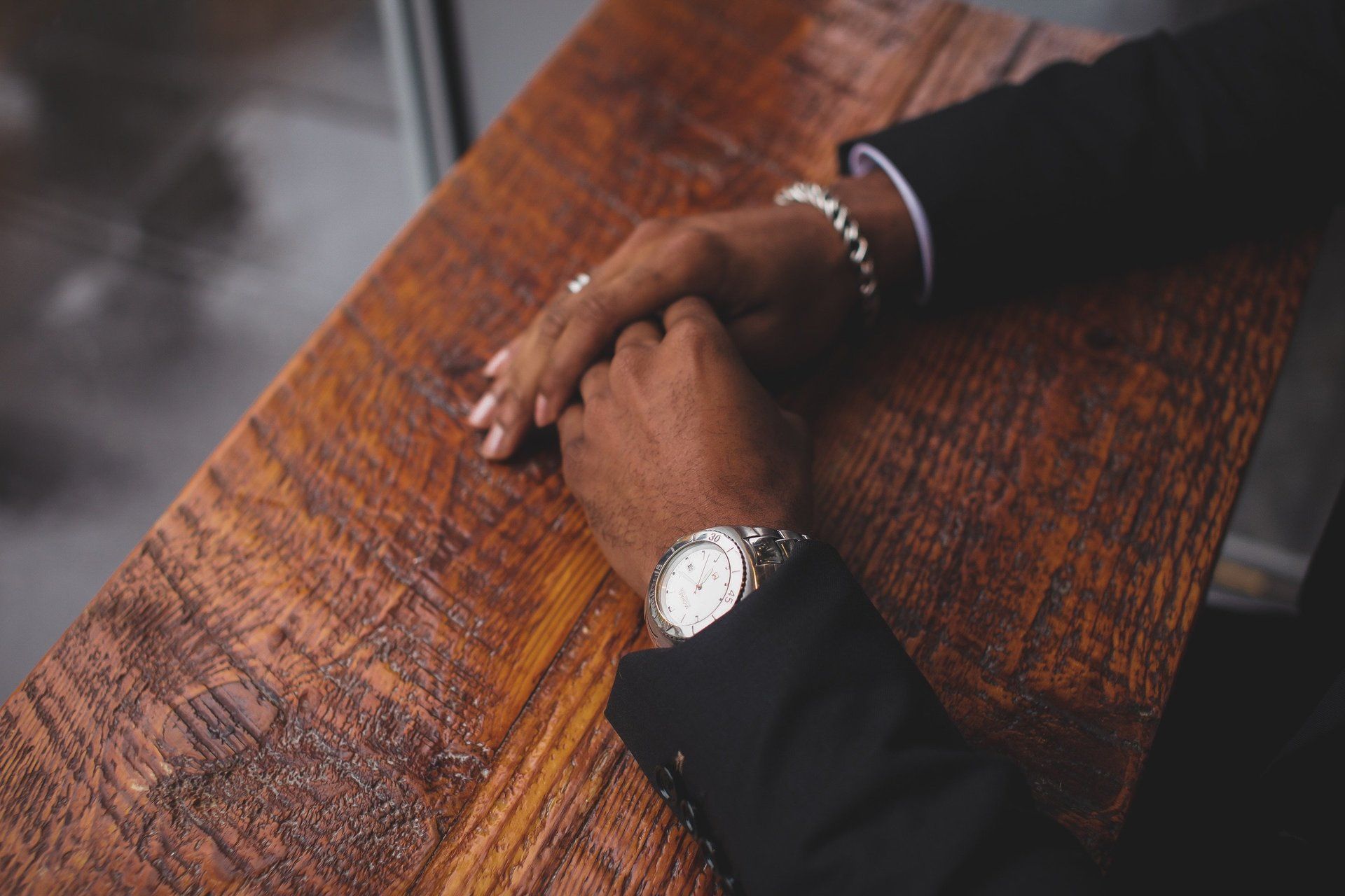 A man wearing a watch and a bracelet is sitting at a wooden table.