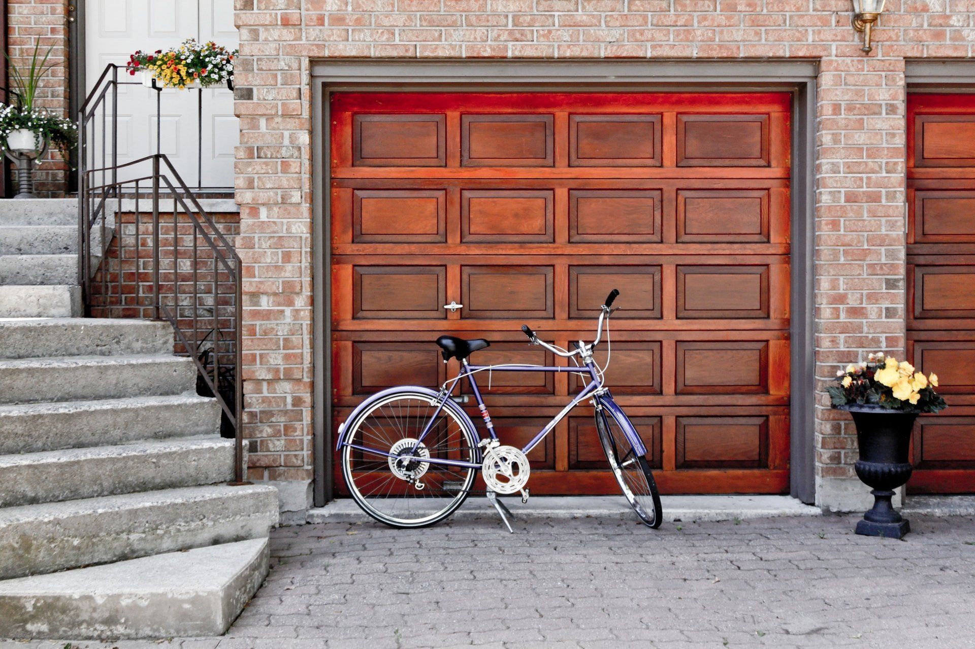 Bicycle parked in front of a wood-paneled garage door; stairs lead up to a house entrance.