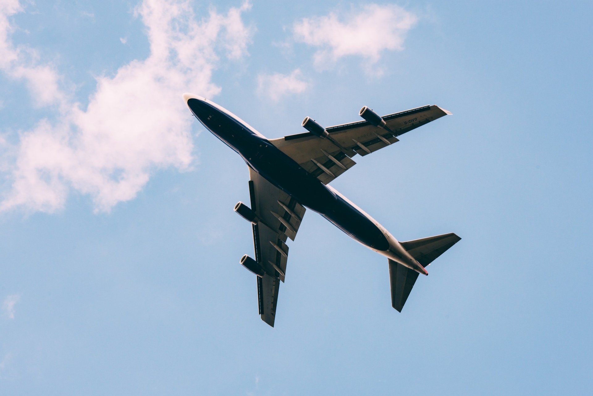 Airplane flying overhead against a blue sky with scattered clouds.