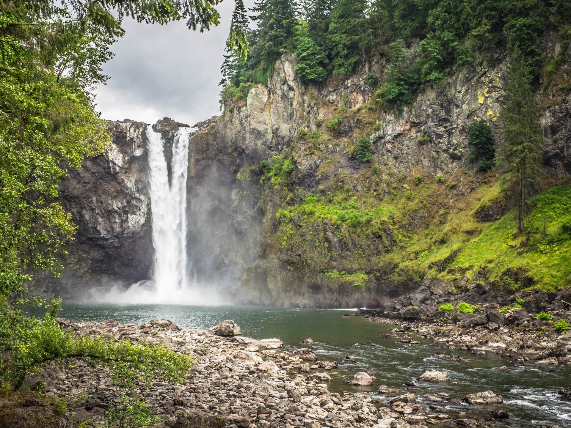 A waterfall is surrounded by trees and rocks in the middle of a river.