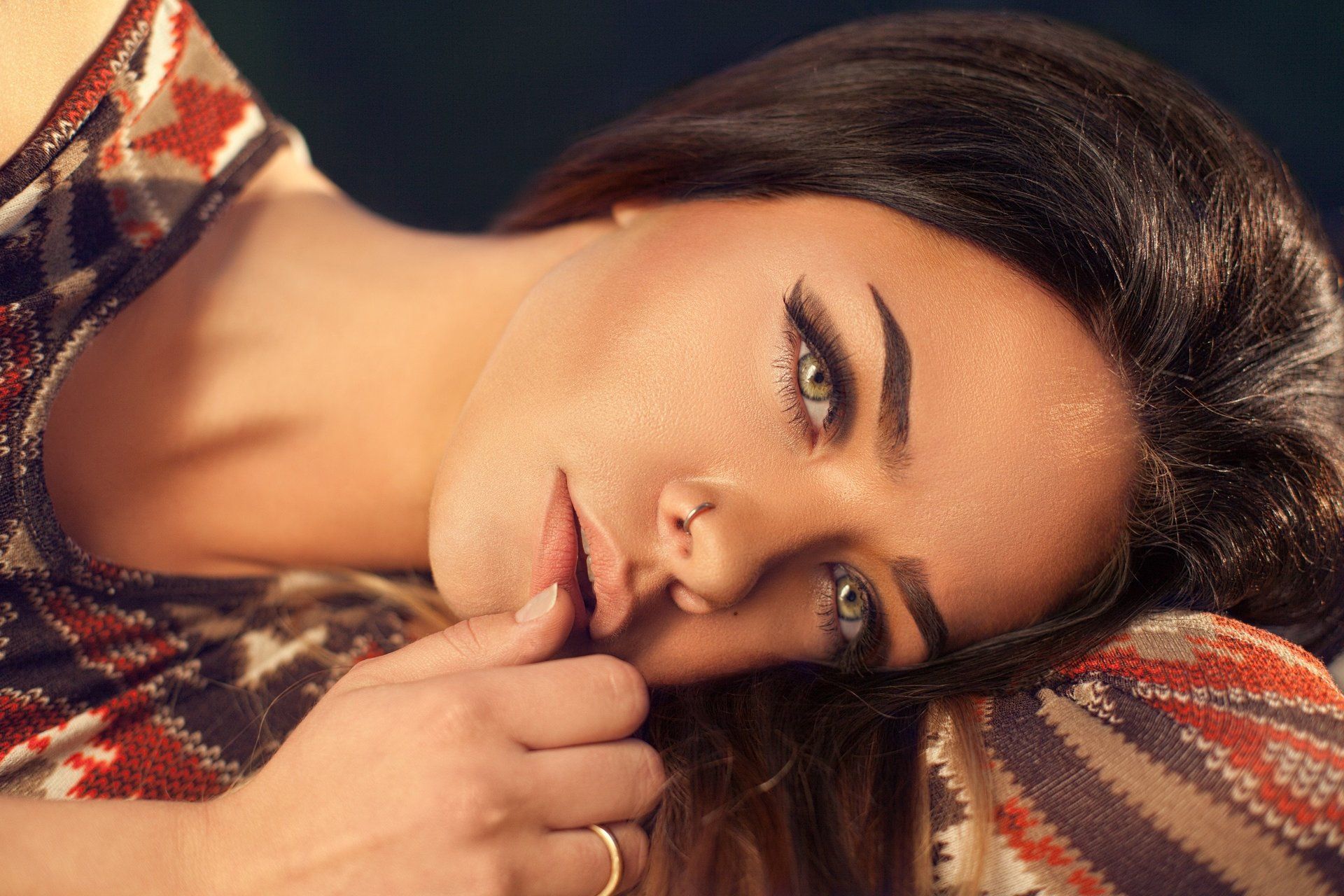 A woman with a nose ring is laying down with her hand on her face.