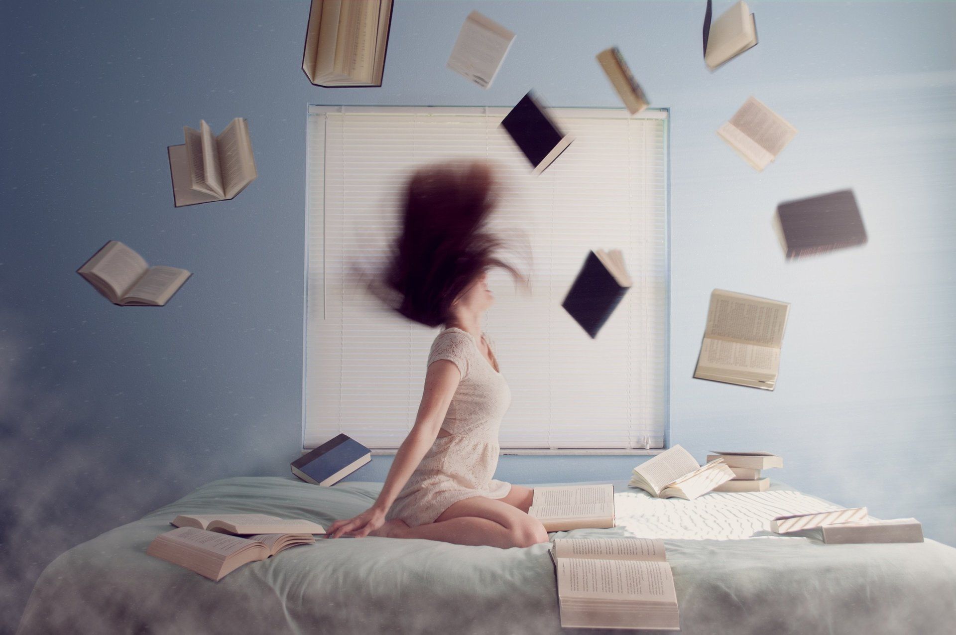 A woman is sitting on a bed with books falling around her.