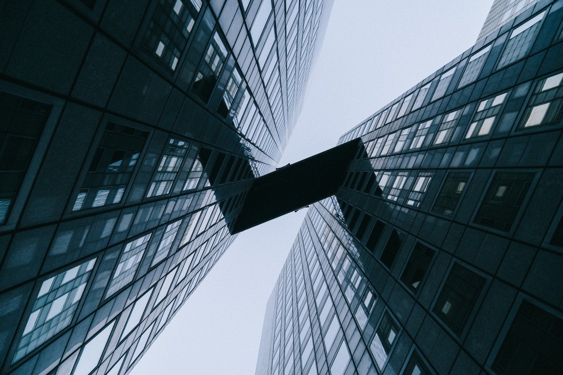 Upward view of glass skyscrapers converging around a dark sky bridge