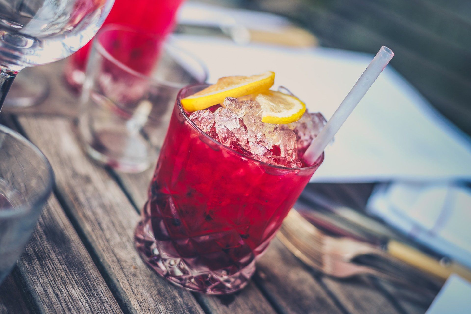 A close up of a red drink with ice and a straw on a wooden table.