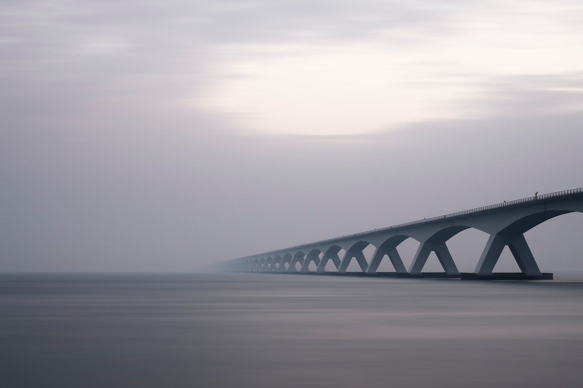 Een lange brug die in de mist verdwijnt boven kalm water.
