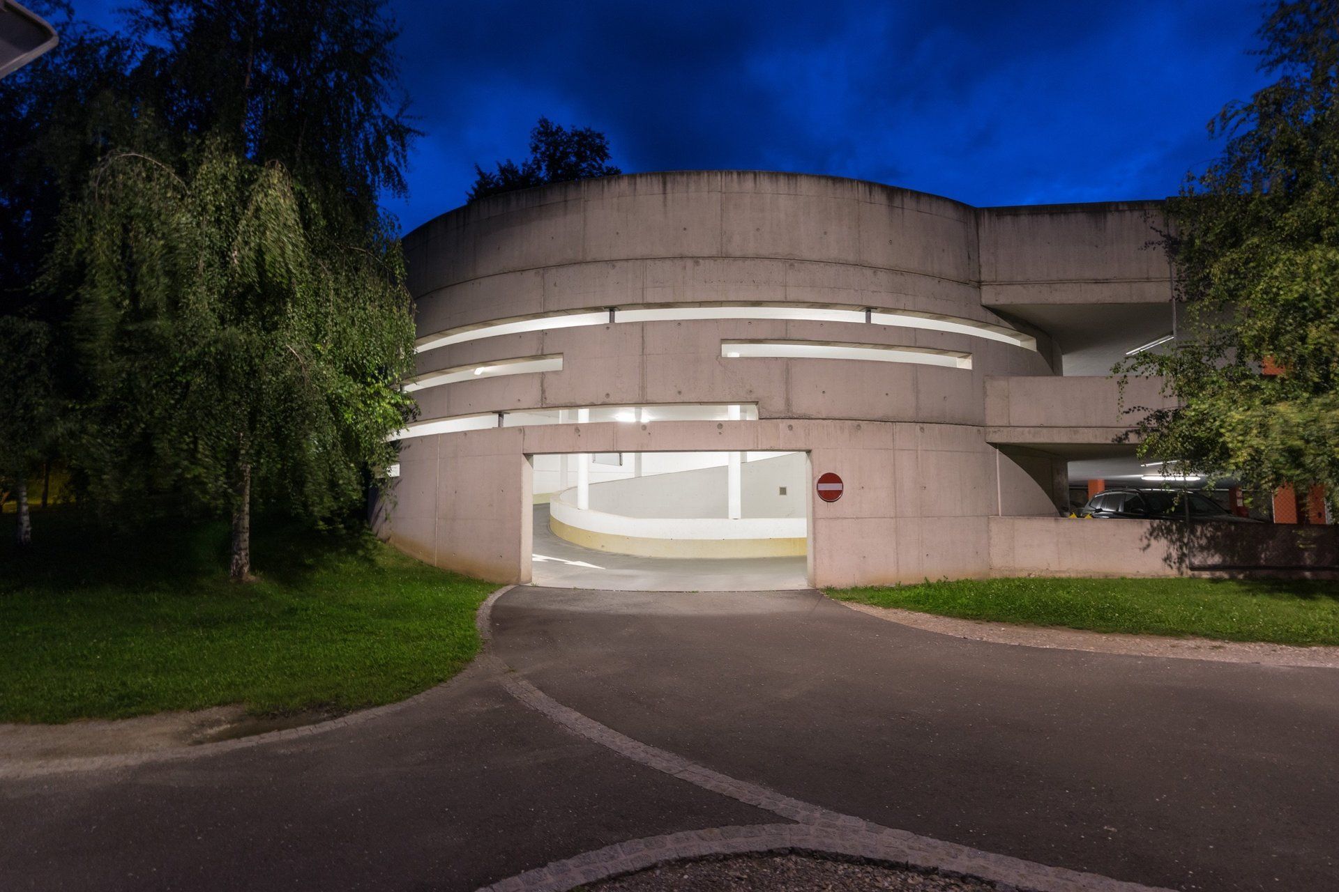 A parking garage is lit up at night with trees in the background.