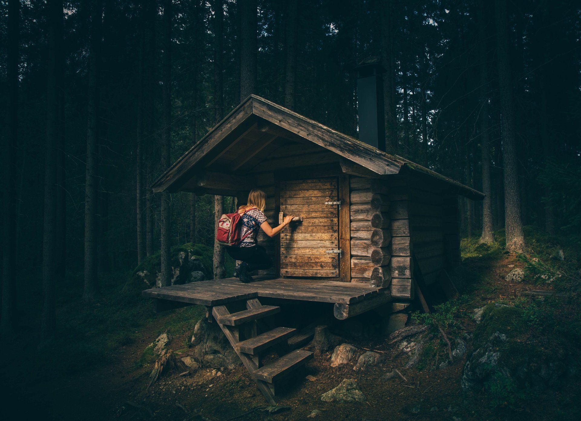 A person is standing in front of a small wooden cabin in the woods.