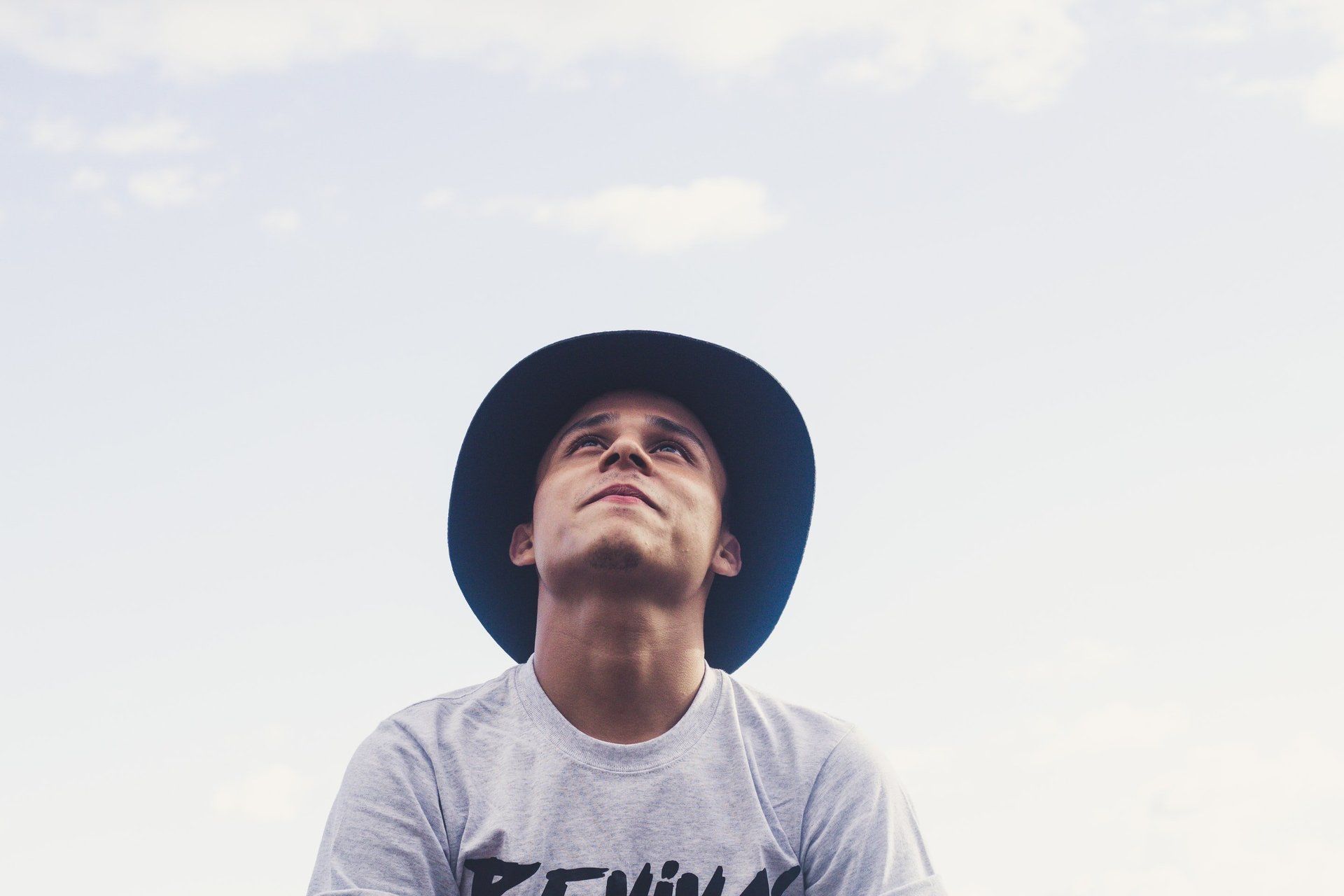 Man in a hat looking up at a partly cloudy sky.