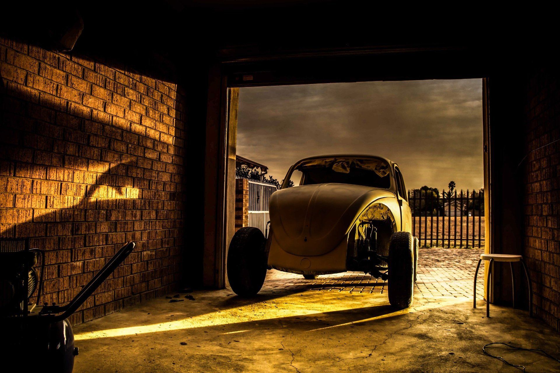 Beetle car in a garage with open door, casting shadows on brick walls. Golden sunlight illuminates the scene.