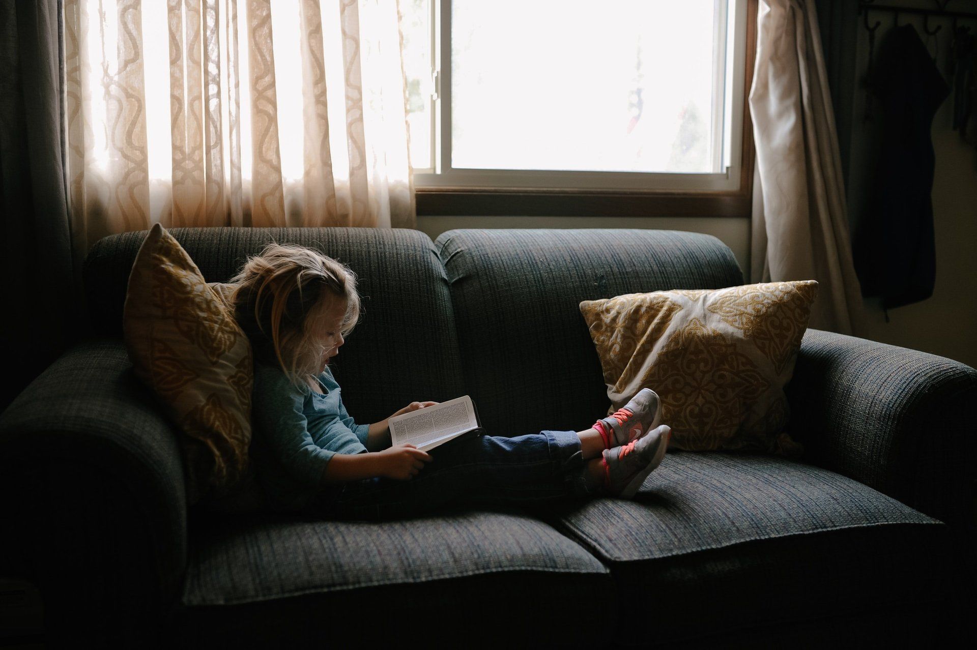 A little girl is sitting on a couch reading a book.
