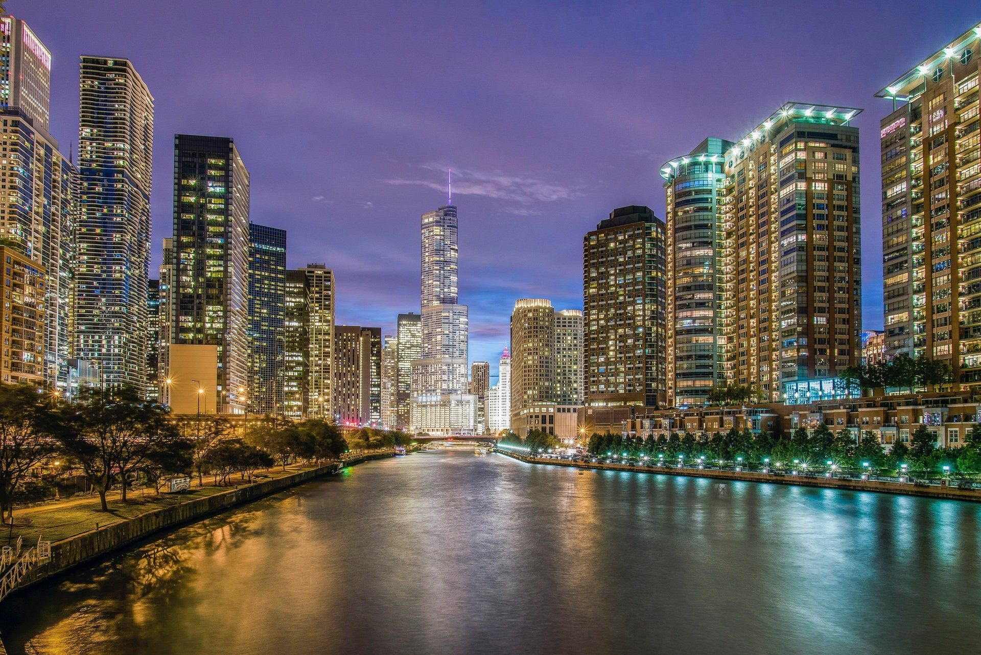 A city skyline at night with a river in the foreground.