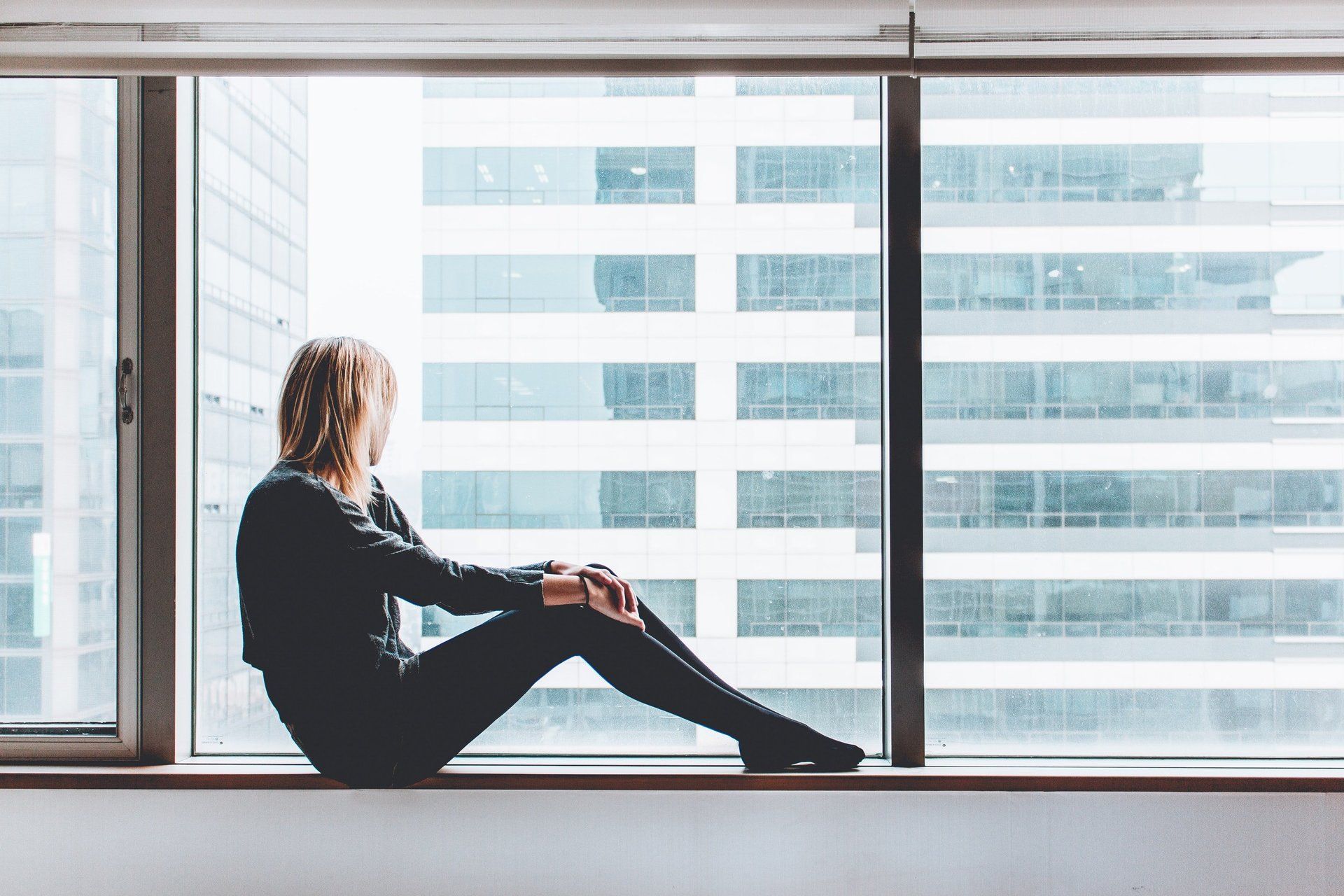A woman is sitting on a window sill looking out the window.