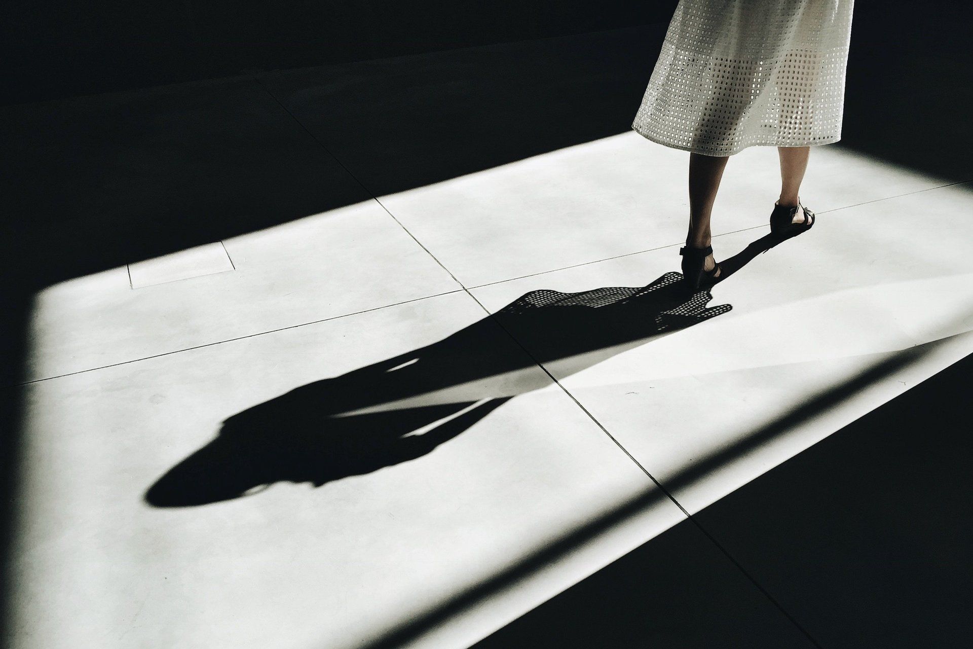 A woman in a white dress is walking and her shadow is cast on the floor