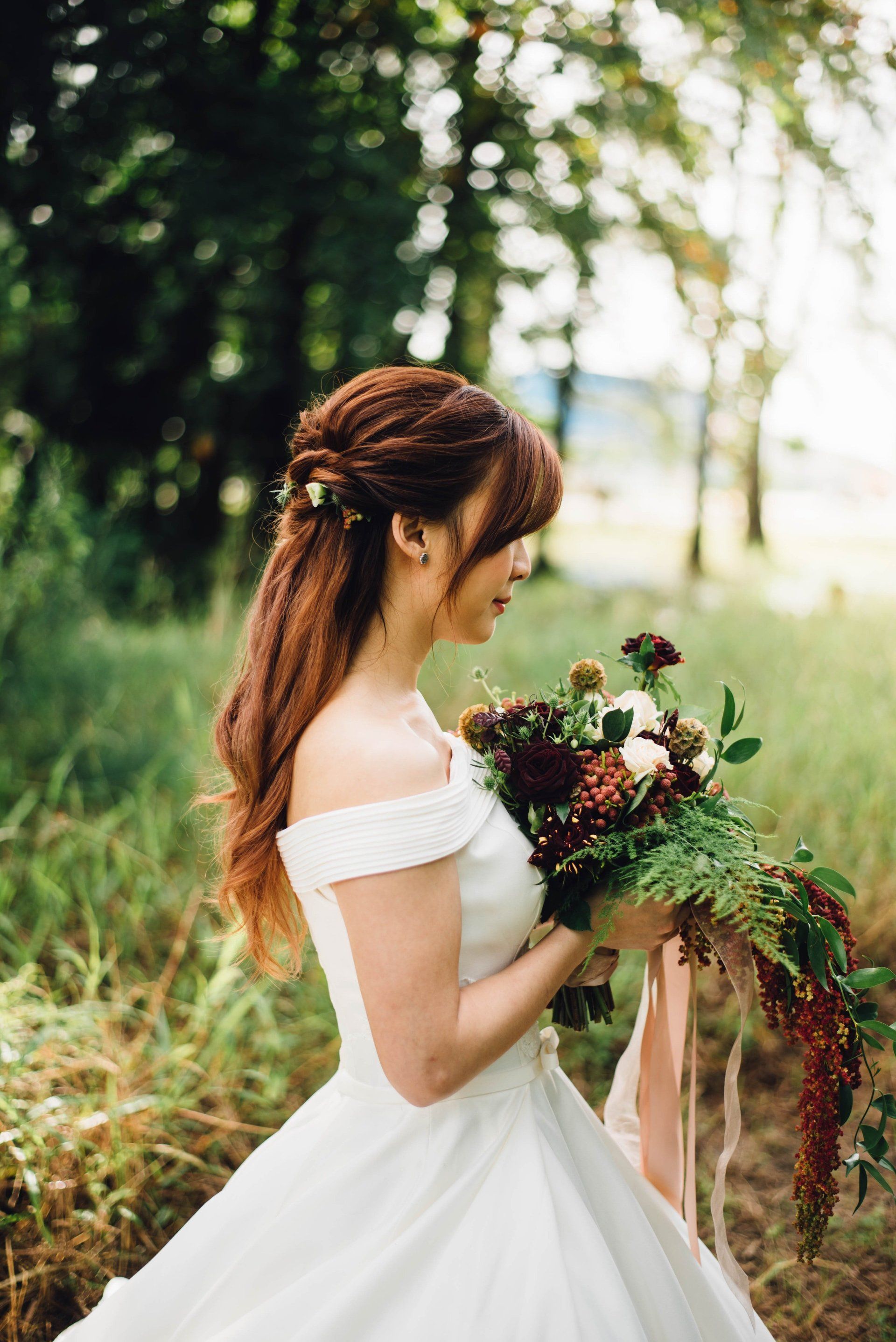 Bride in white dress, holding bouquet, in a field, hair up with flowers.