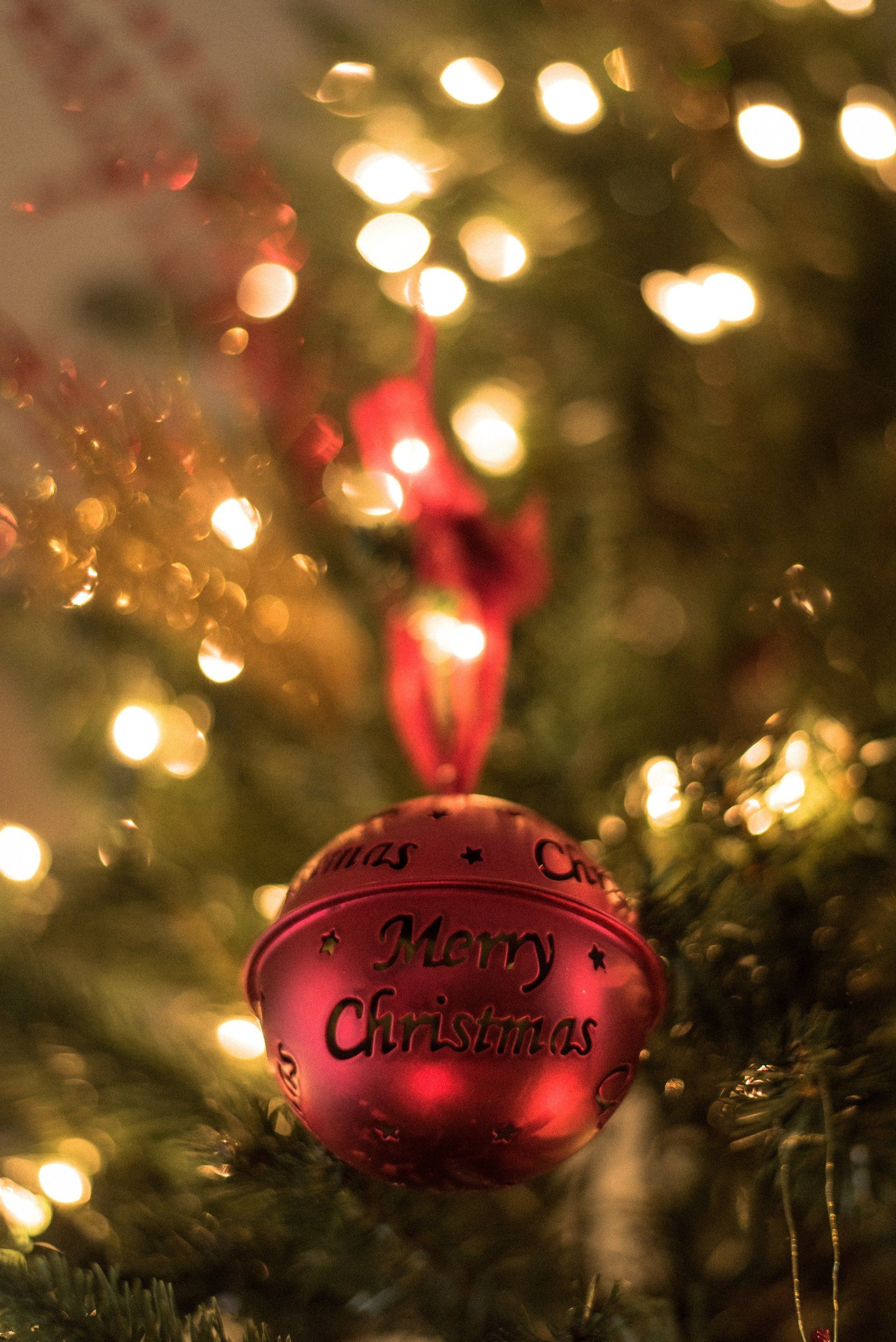 A red christmas bell is hanging from a christmas tree.