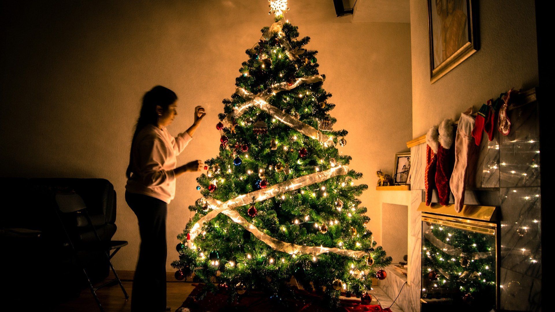 A woman is decorating a christmas tree in a living room.