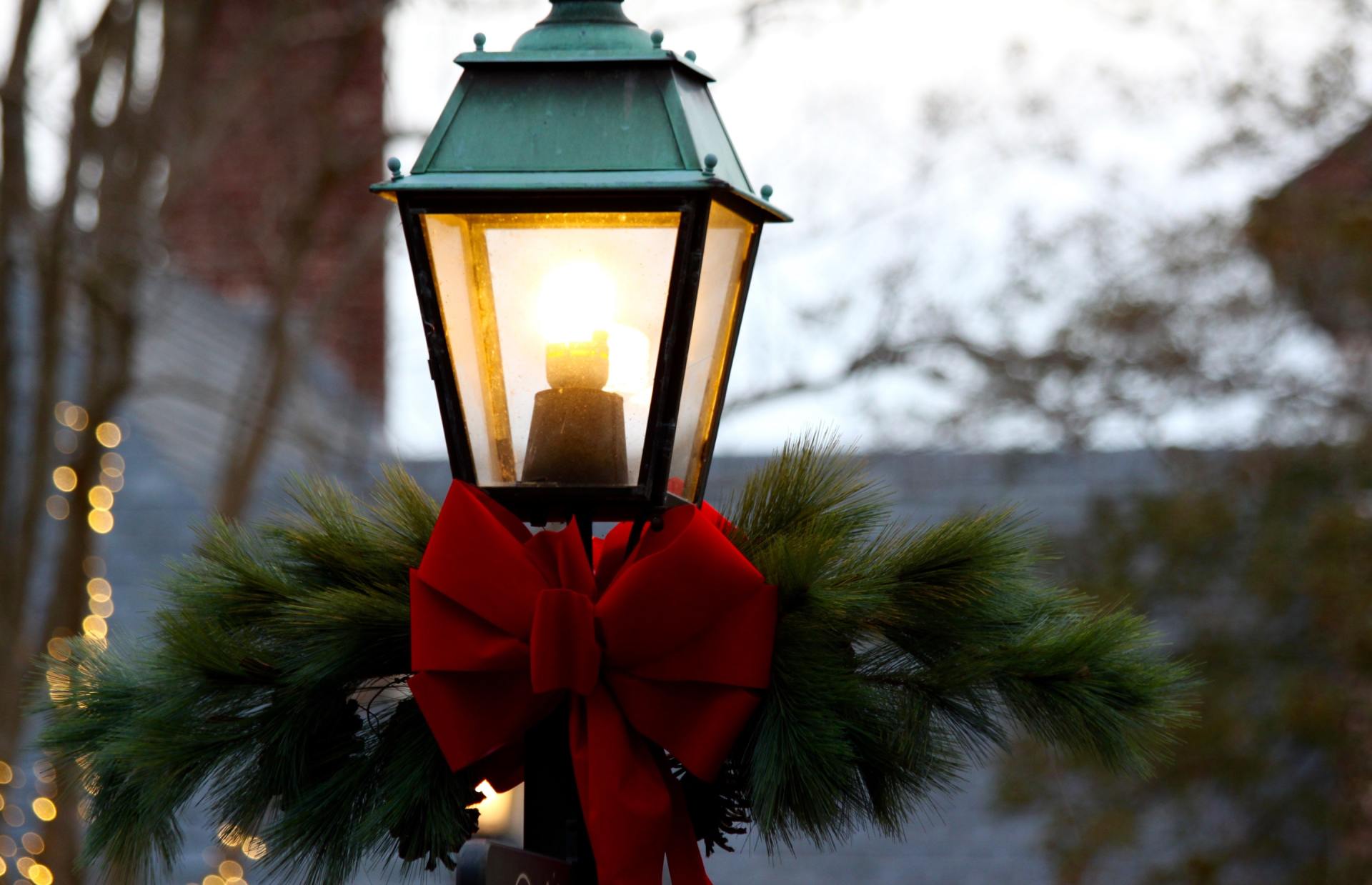 Lamp post with green top, red bow, and pine boughs, lit at dusk.