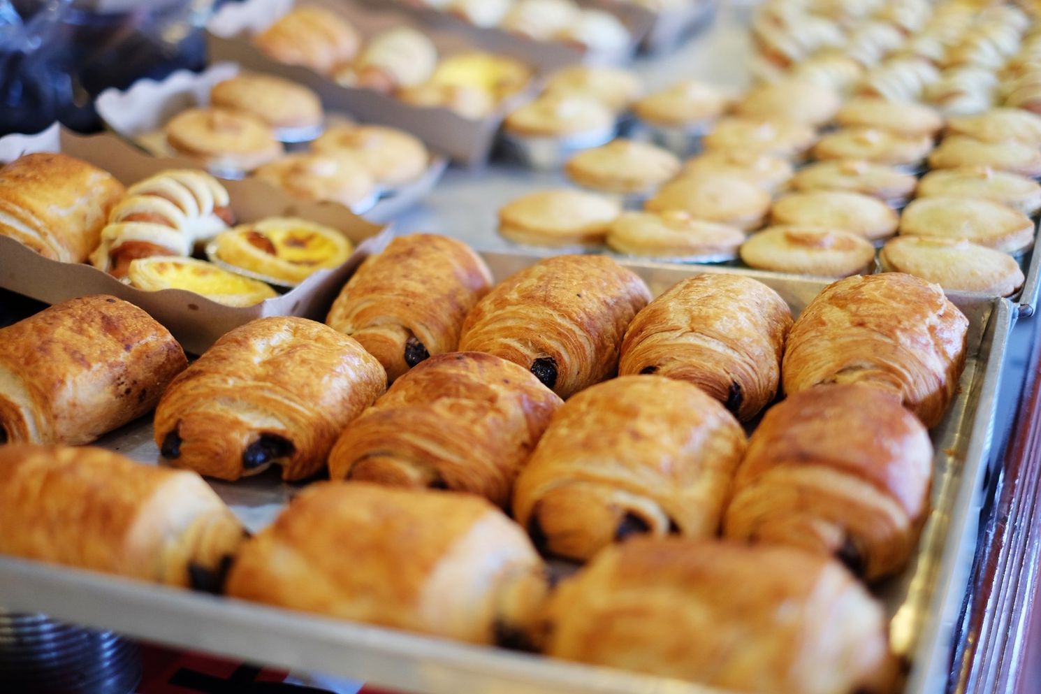 Assortment of baked pastries: croissants, tarts, and rolls, displayed on trays in a bakery setting.