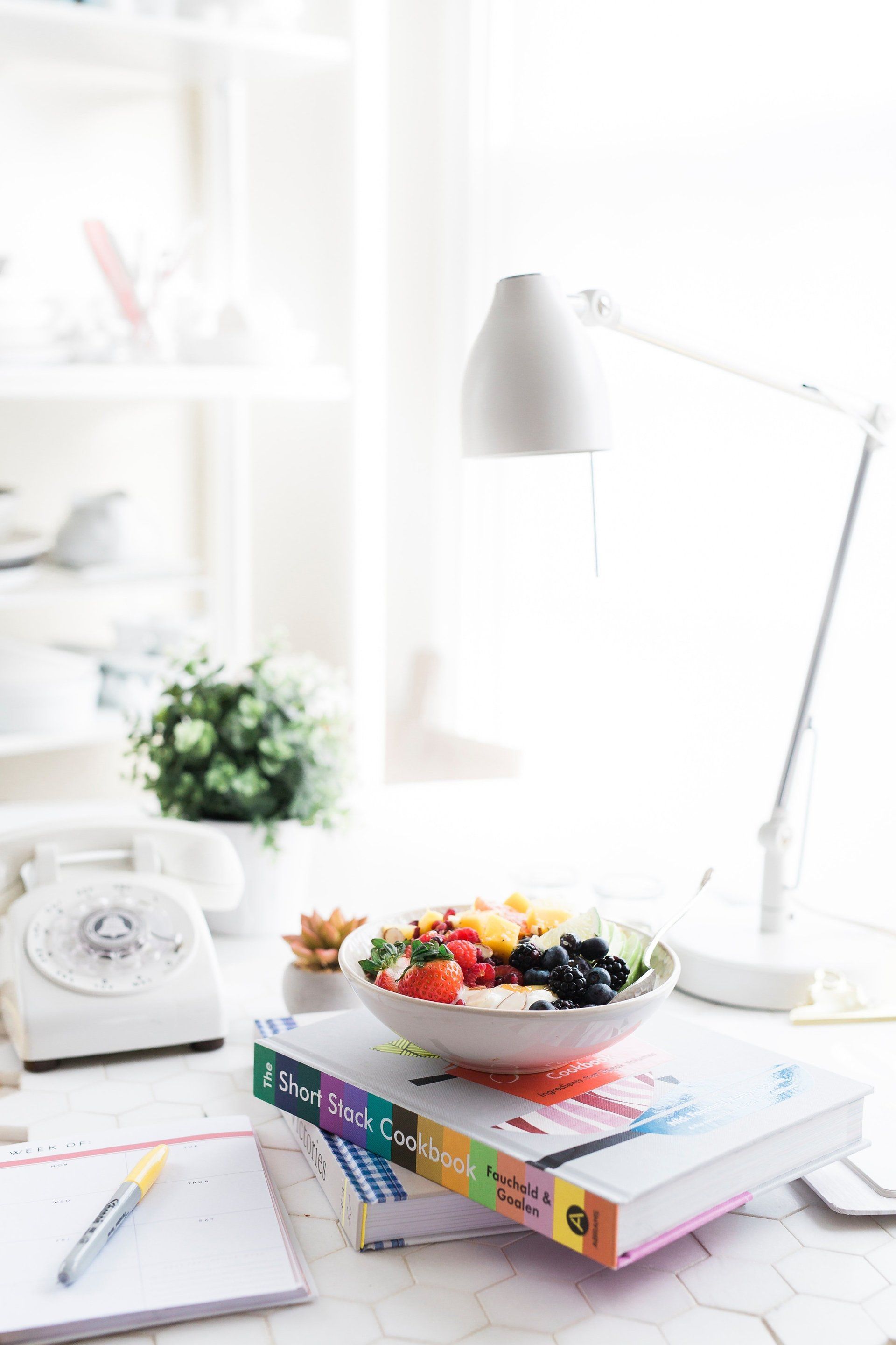 A bowl of fruit is sitting on top of a stack of books on a desk.