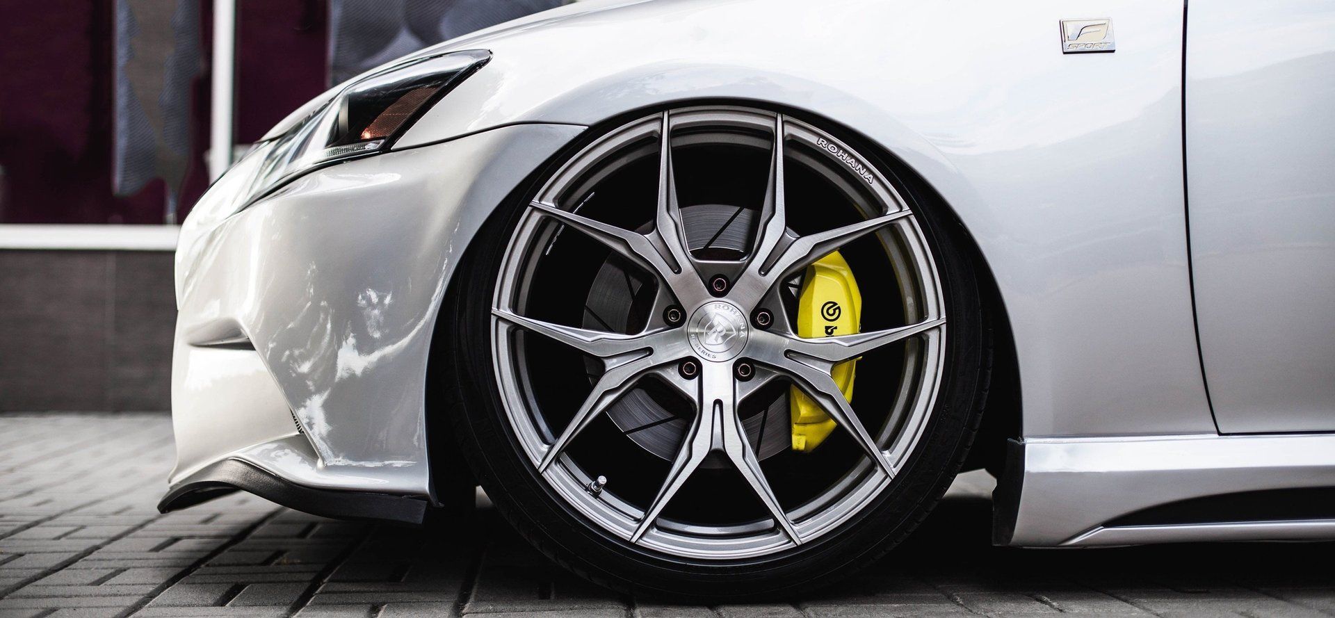 A silver car with yellow brake calipers is parked on a sidewalk.