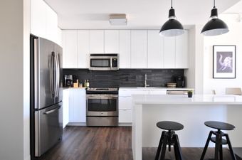 Modern kitchen with stainless steel appliances, white cabinets, black backsplash, and a breakfast bar with stools