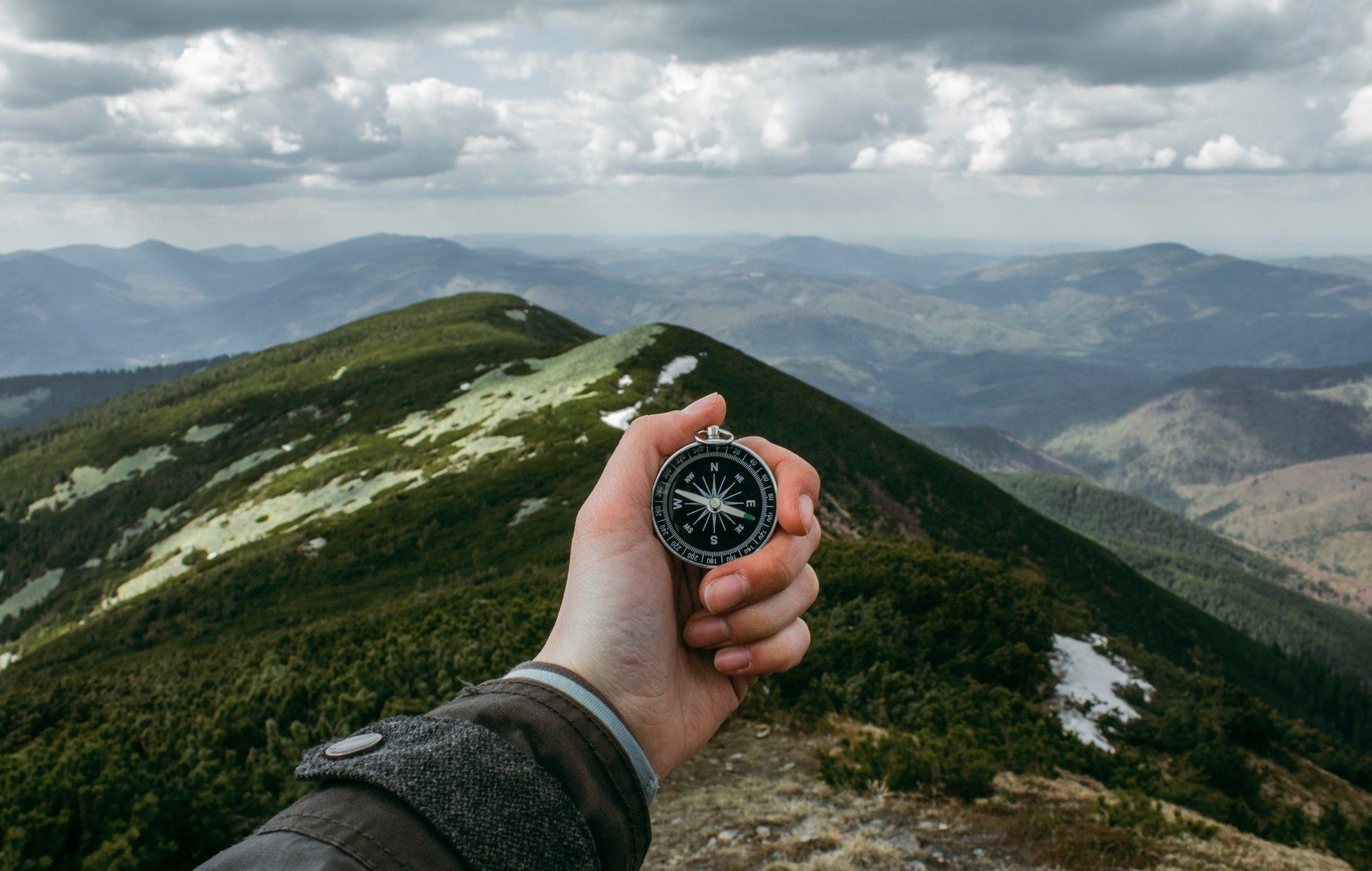 A person is holding a compass in front of a mountain.