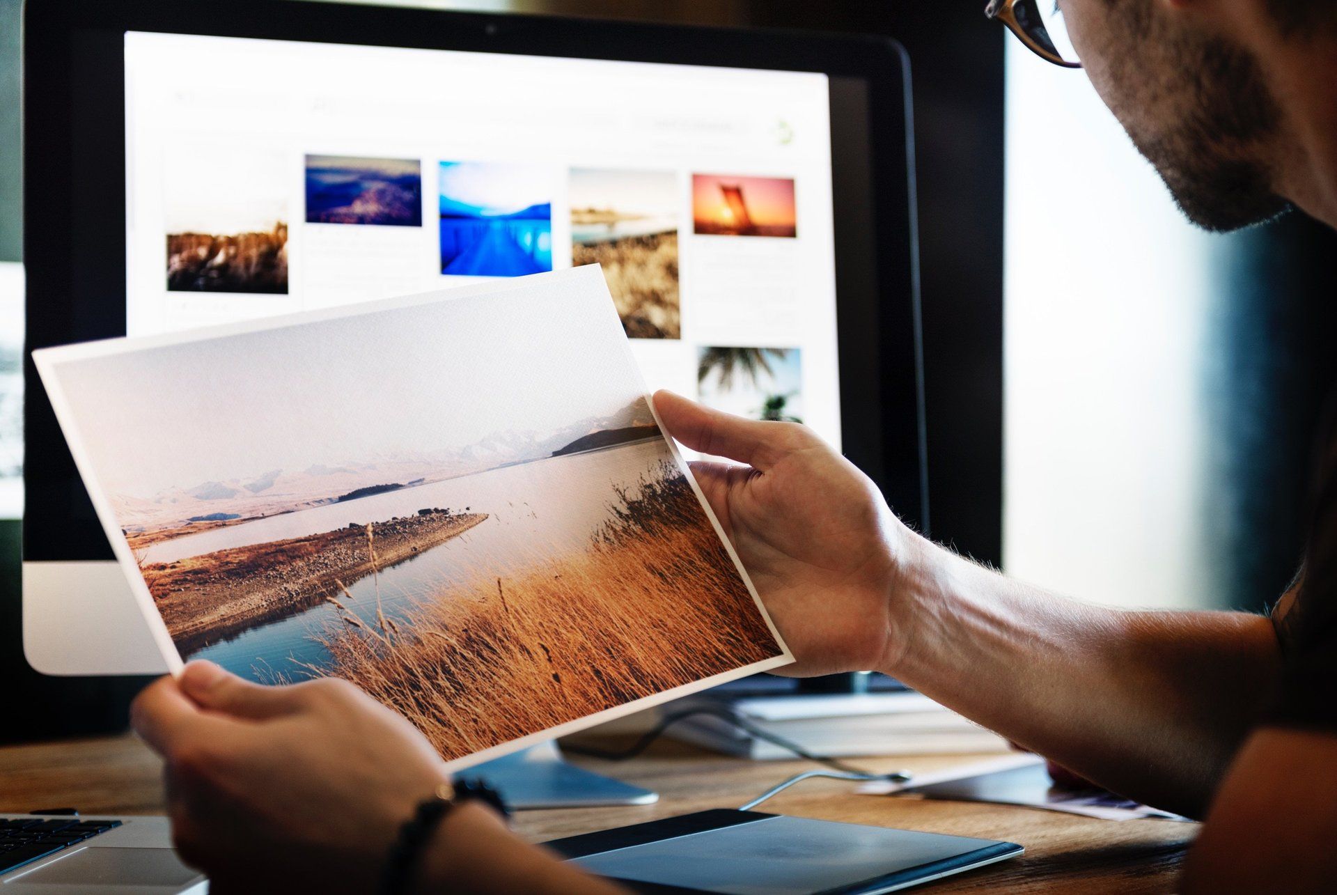 A man is holding a picture in front of a computer screen.