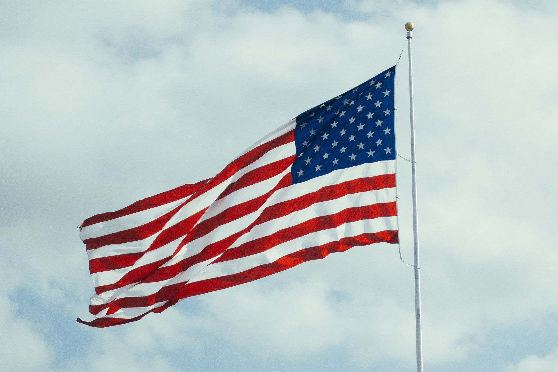 An american flag is flying in the wind against a cloudy sky